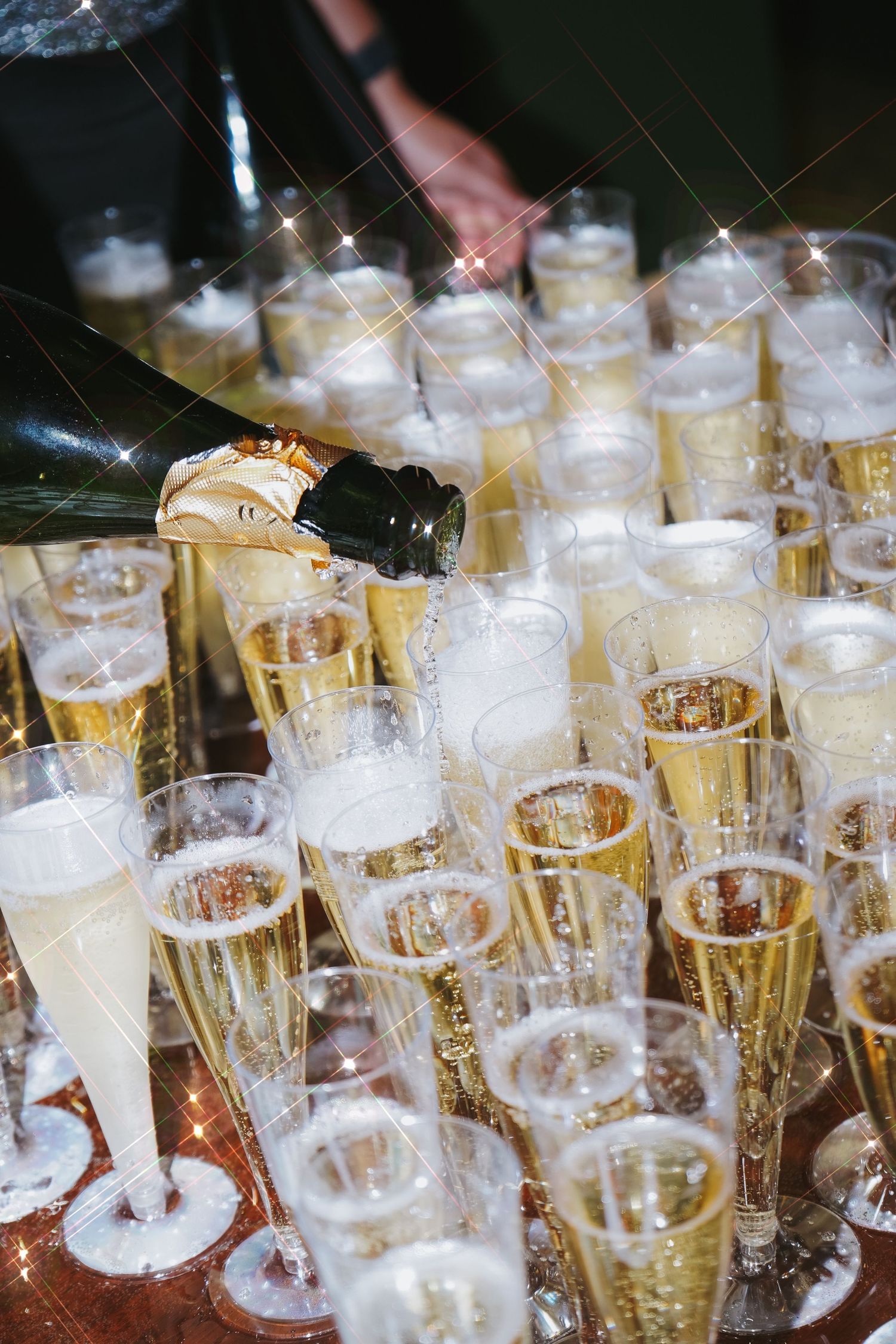 Champagne being poured into multiple glass flutes at an elegant event.