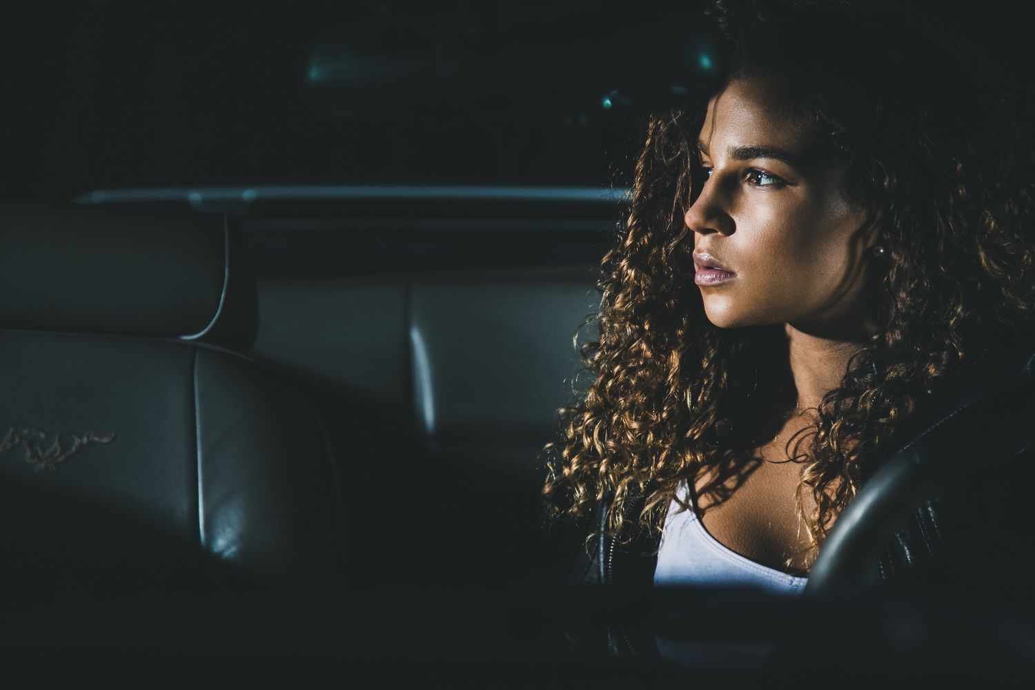 Profile view of person with curly hair sitting in car interior at night.