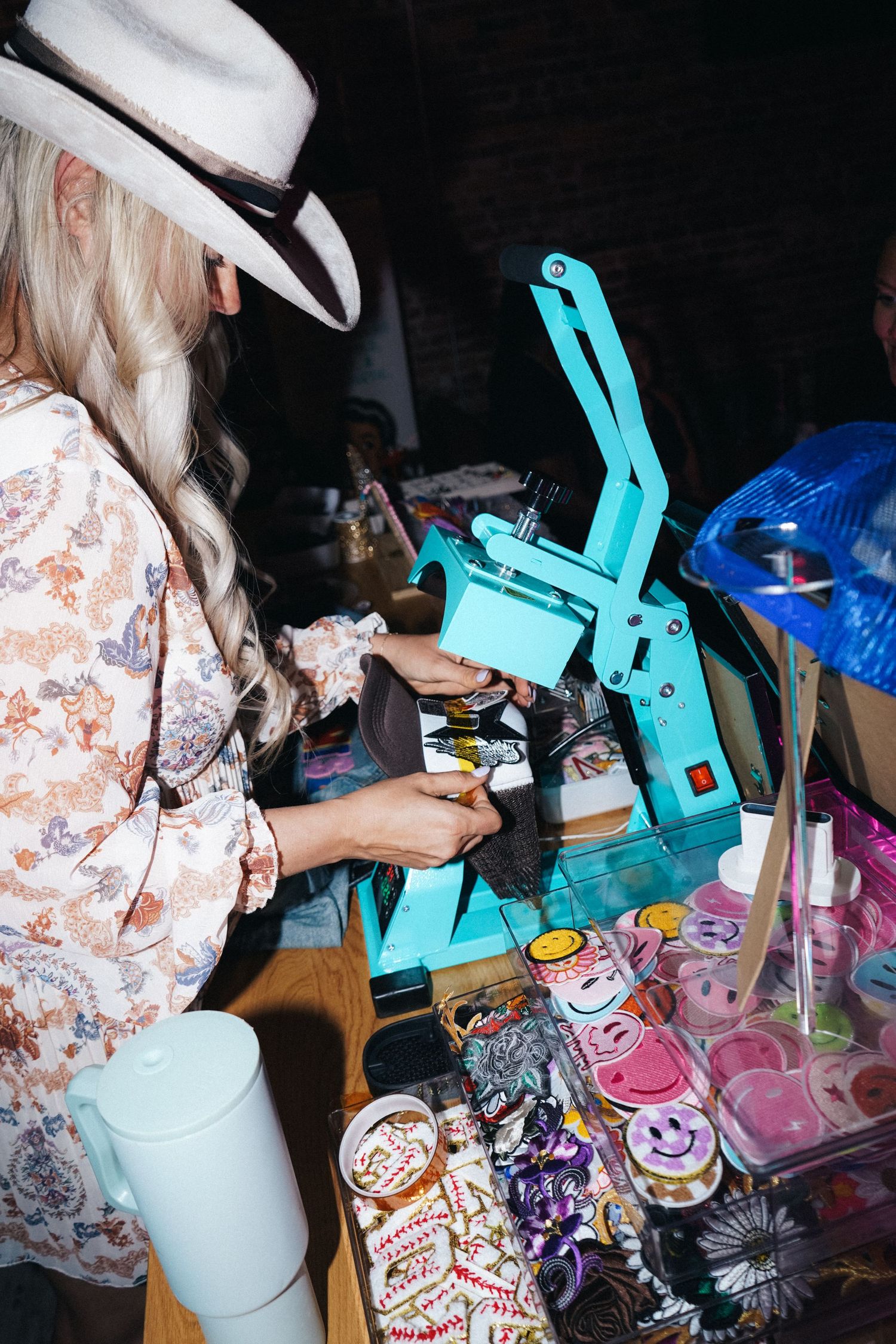 Person in white hat operating turquoise crafting machine with supplies nearby.