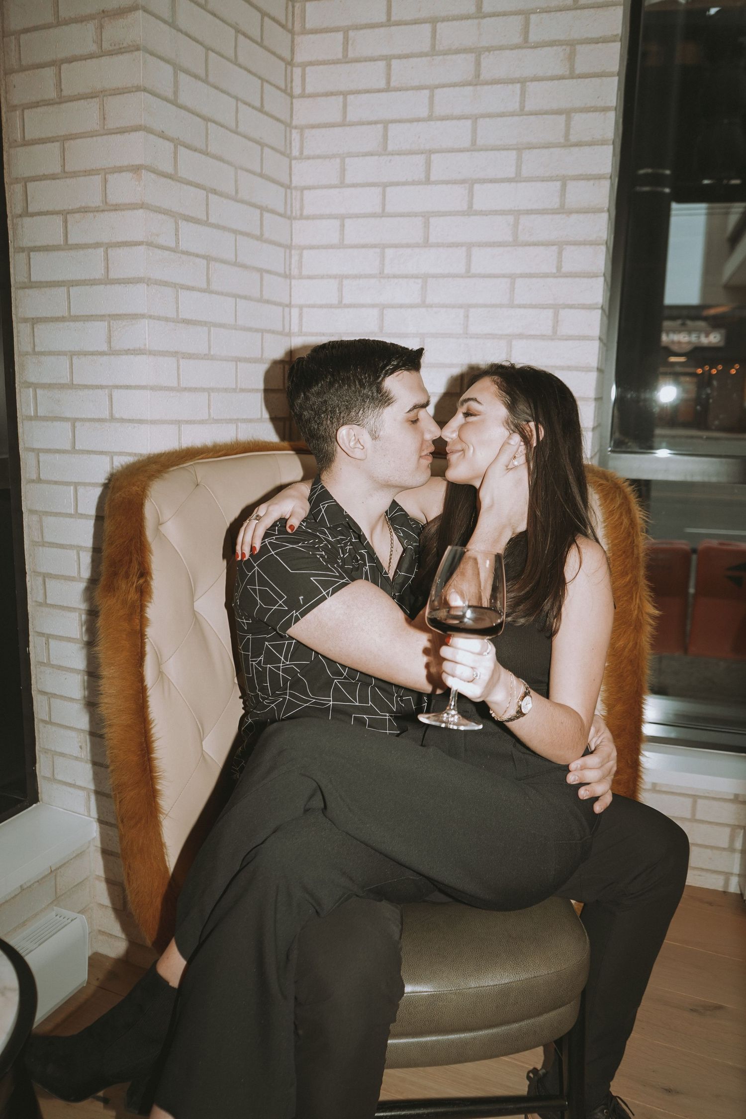 Romantic couple sharing intimate moment with wine on leather chair.