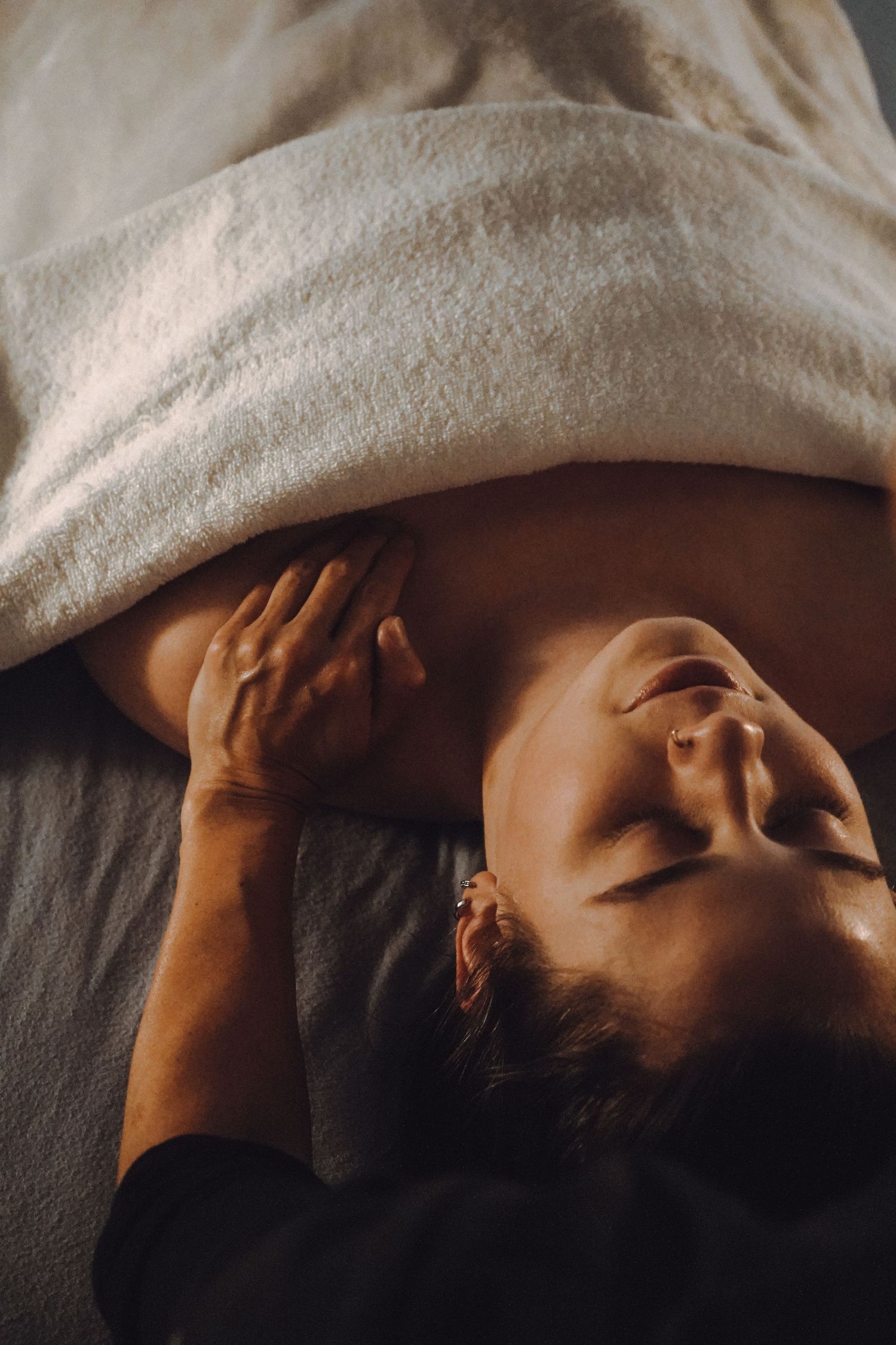 Person receiving relaxing facial massage treatment on dark surface.