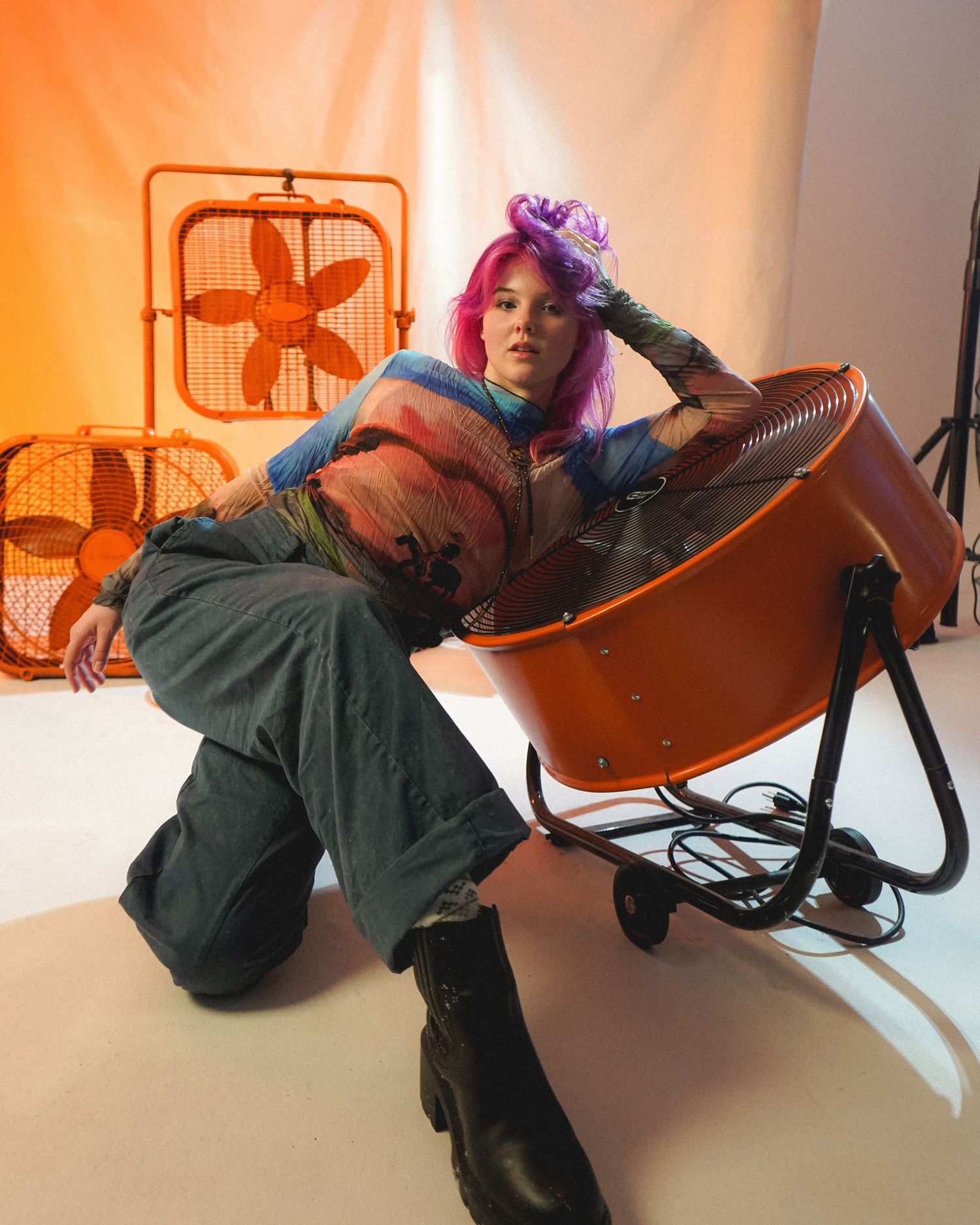 Model with pink hair poses dramatically with industrial fans in urban fashion shoot.