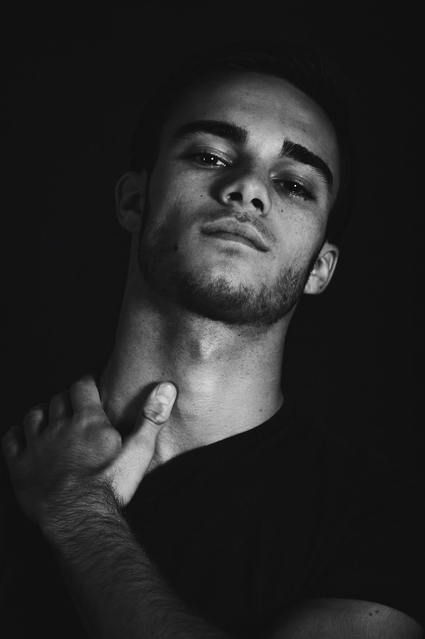 Dramatic black and white portrait with moody lighting showing contemplative expression against dark background.