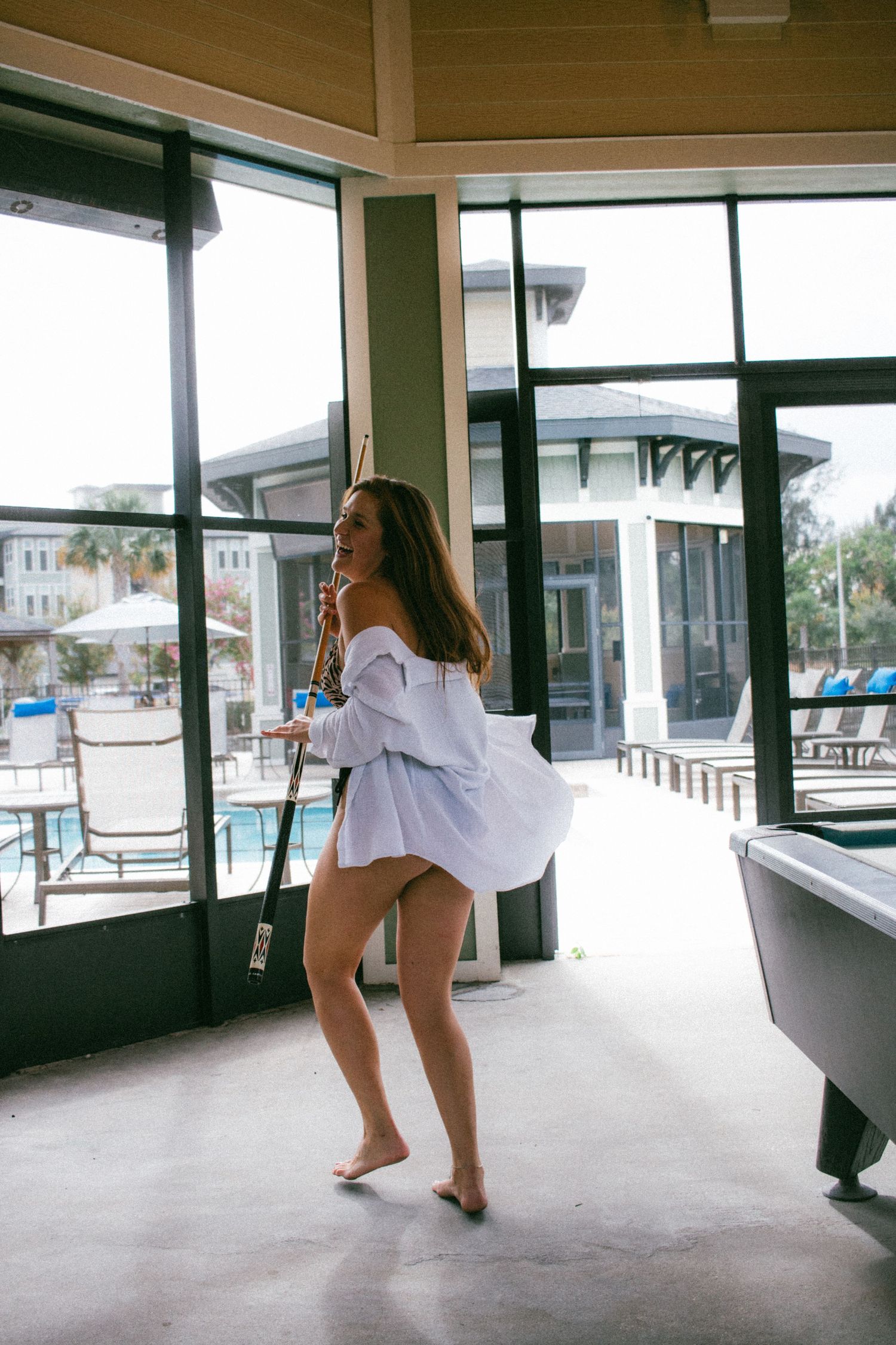 Candid shot of someone dancing in white oversized shirt by sunlit windows.