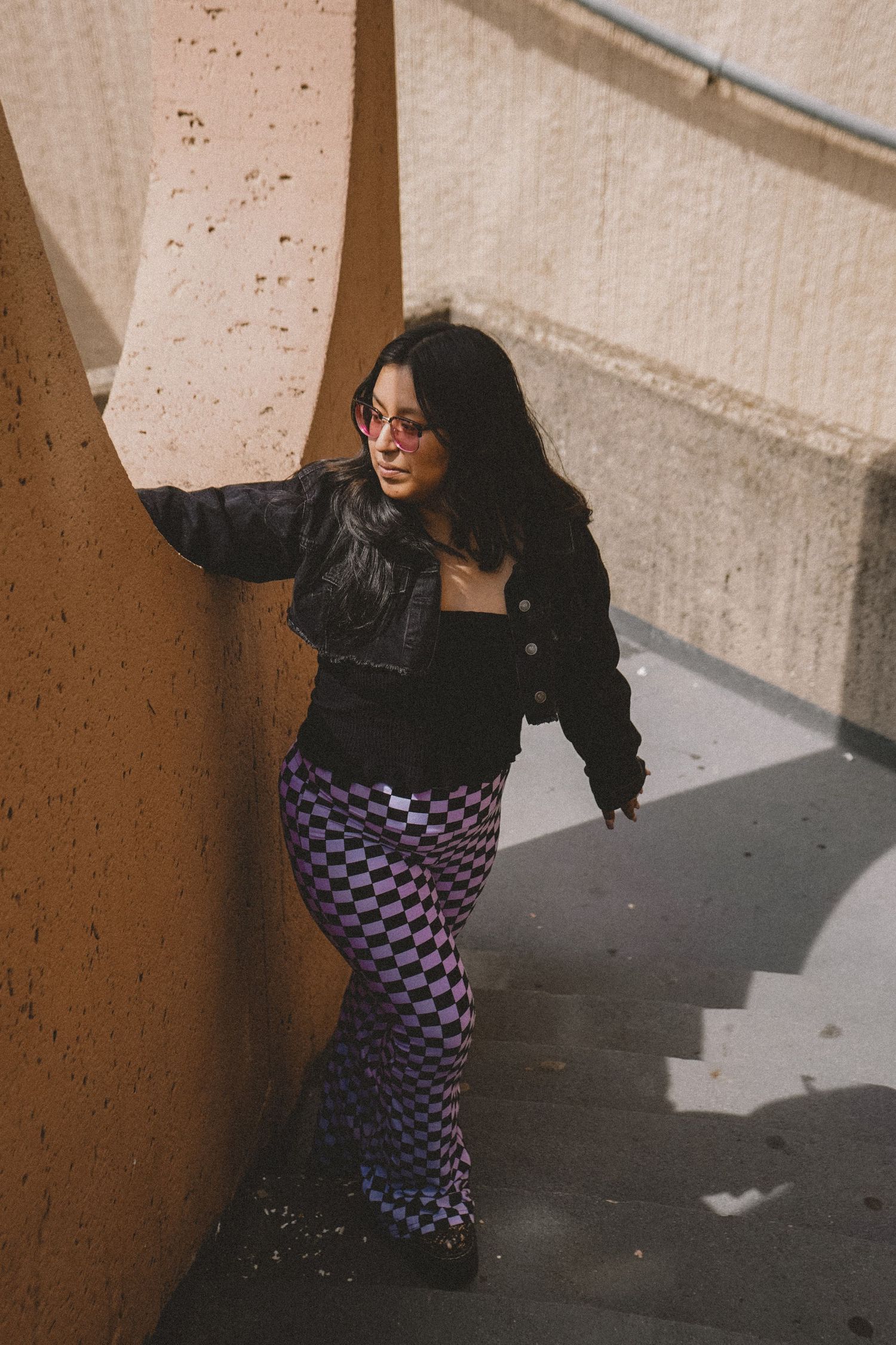 Stylish pose against concrete wall wearing checkered pants and black jacket.