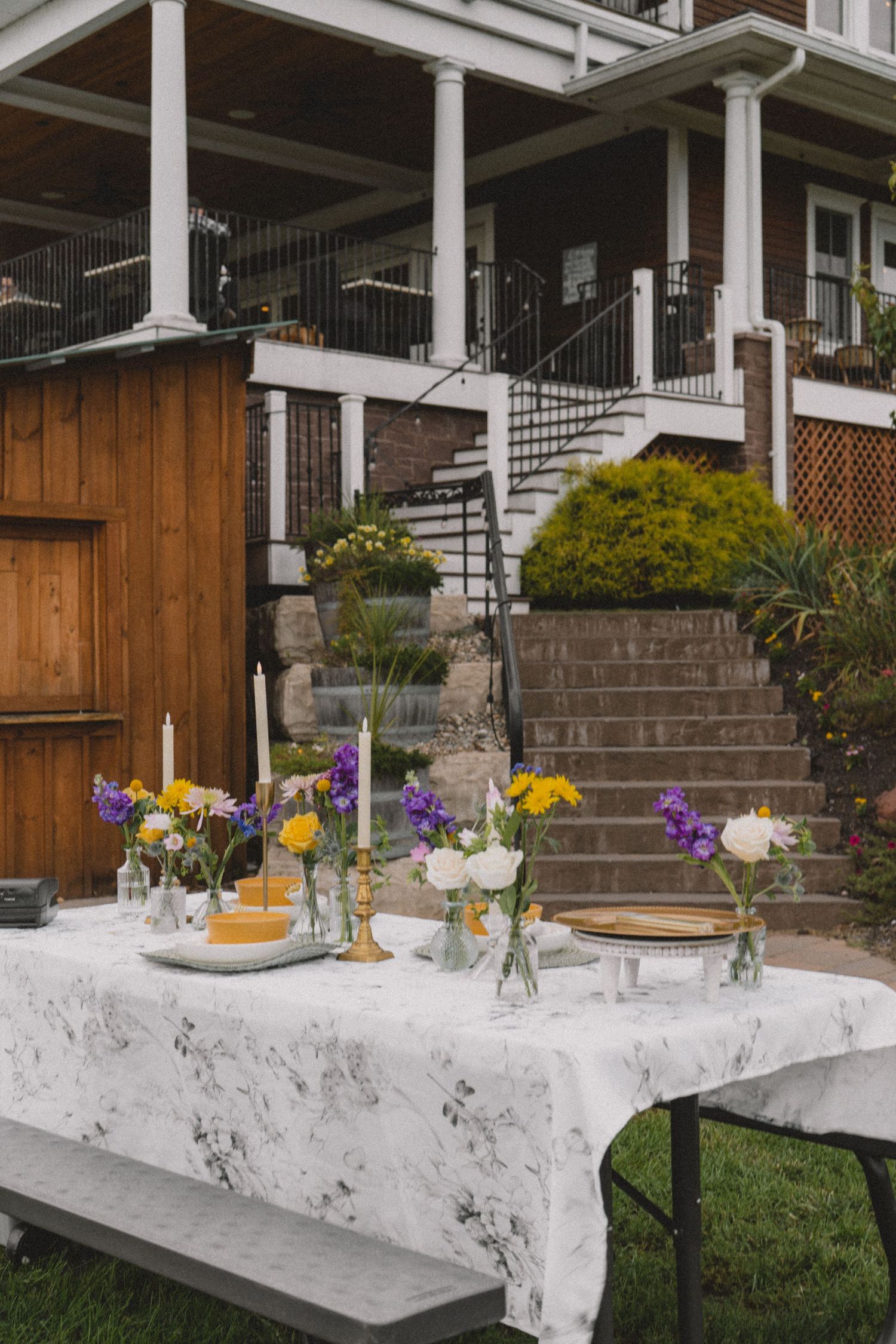 Elegant garden party table setting with fresh flowers and white tablecloth against a house exterior.