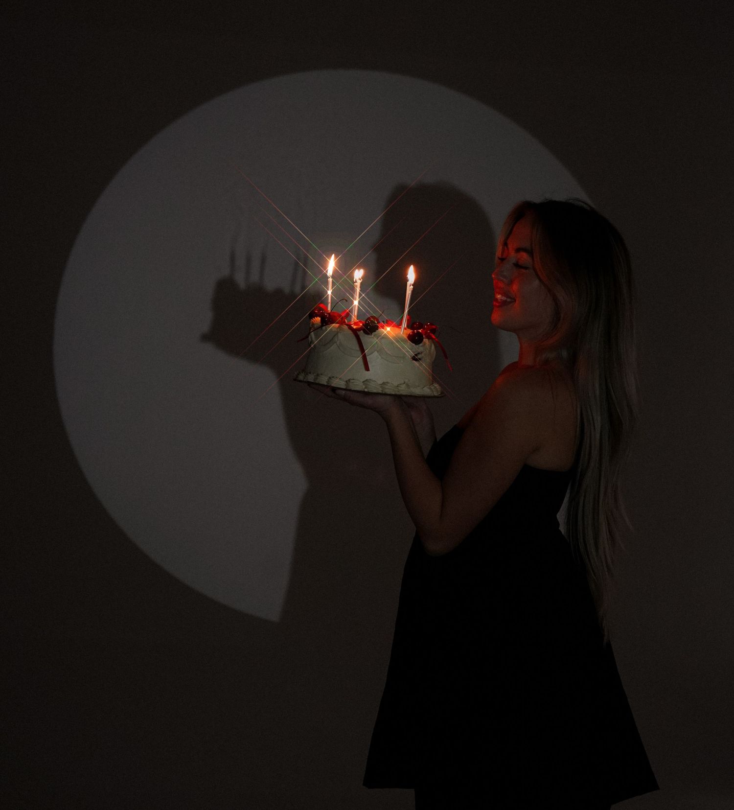 Silhouetted figure blowing out candles on birthday cake in dark room.