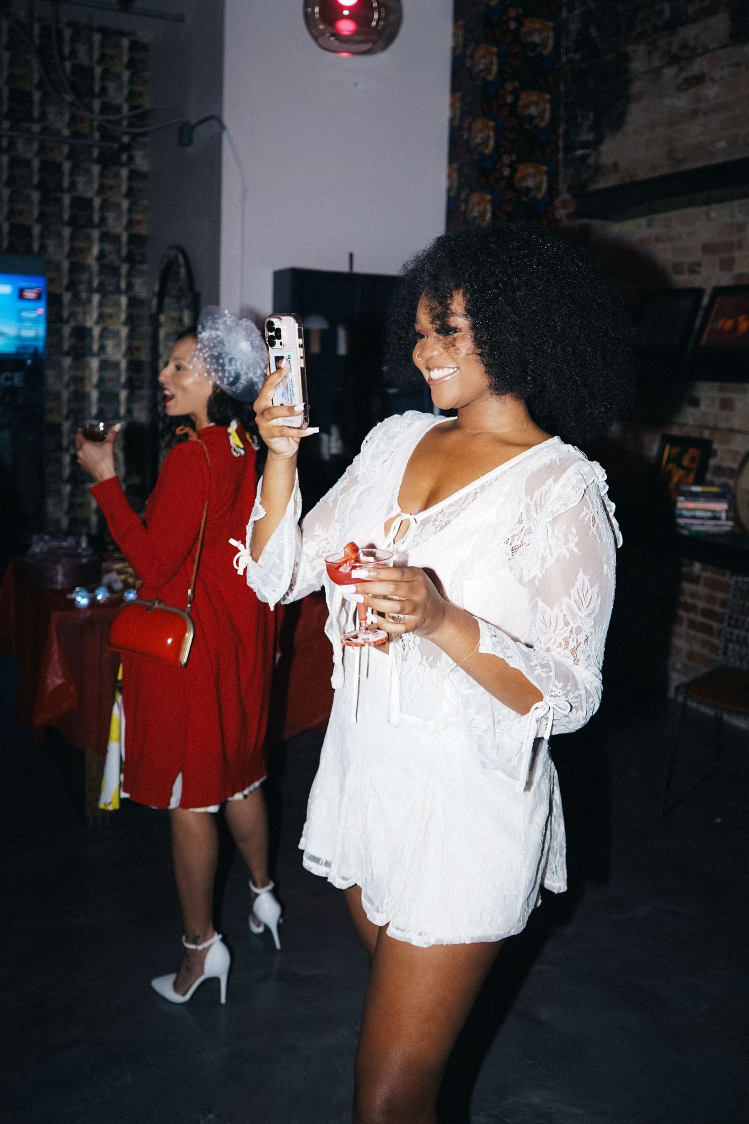 Two friends enjoying drinks and laughing at a party in casual attire.