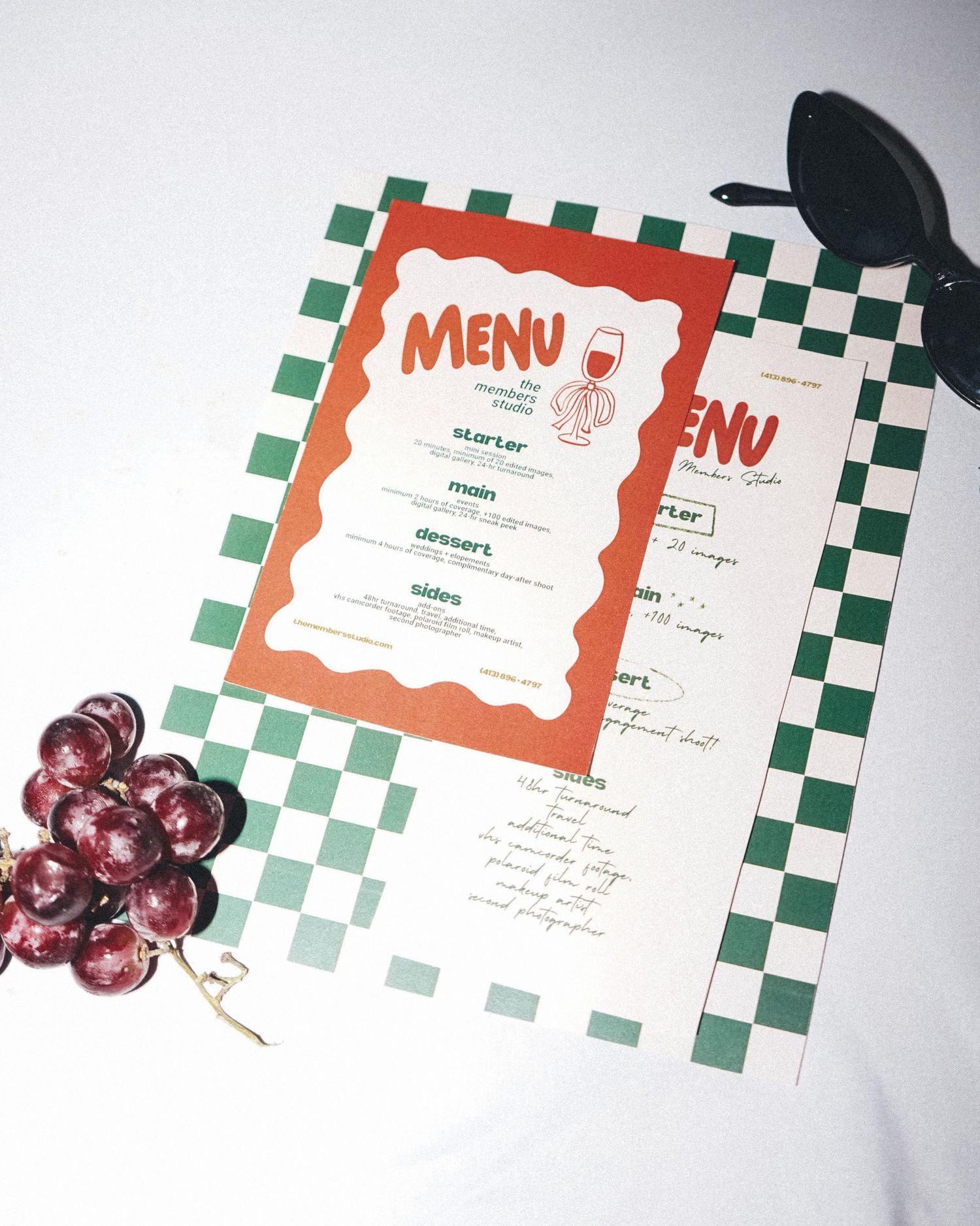 Restaurant menu with green checkerboard border and orange frame displayed with decorative grapes.