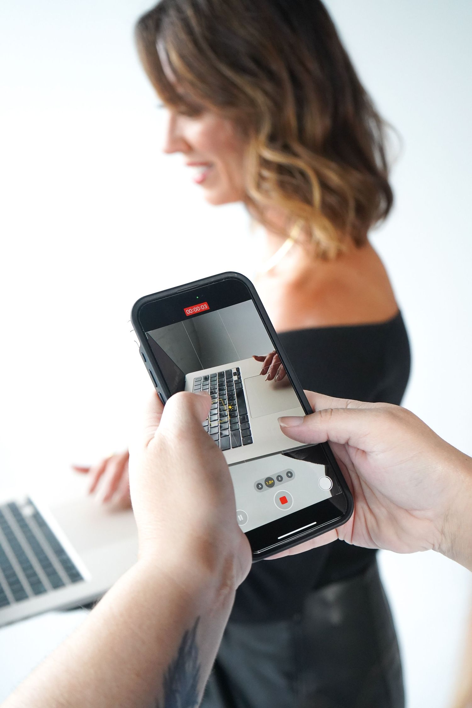 Person using smartphone while working with laptop in background.