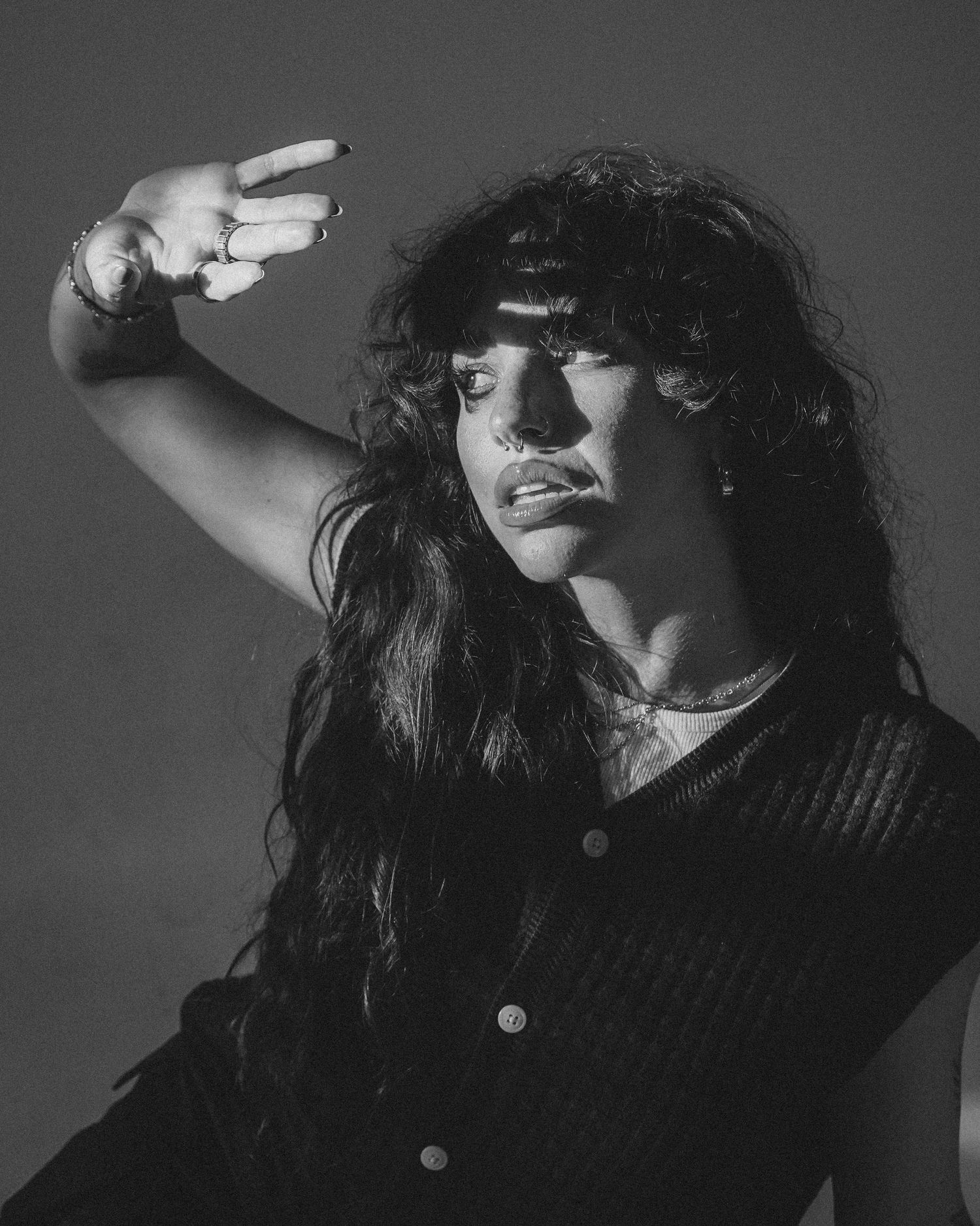 Dramatic black and white portrait with figure making gesture against moody backdrop.
