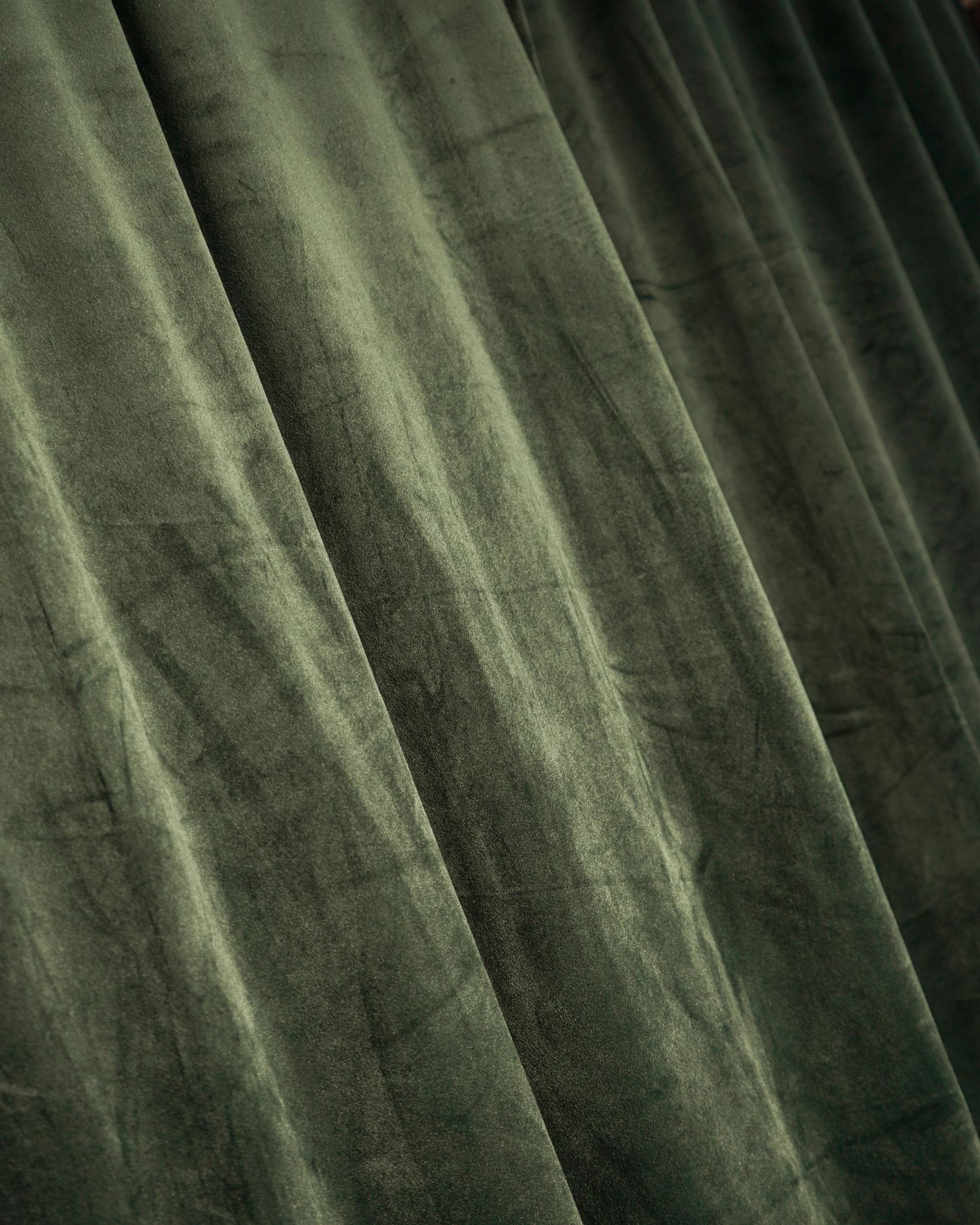 Close-up texture of deep green velvet fabric with dramatic folds and shadows.