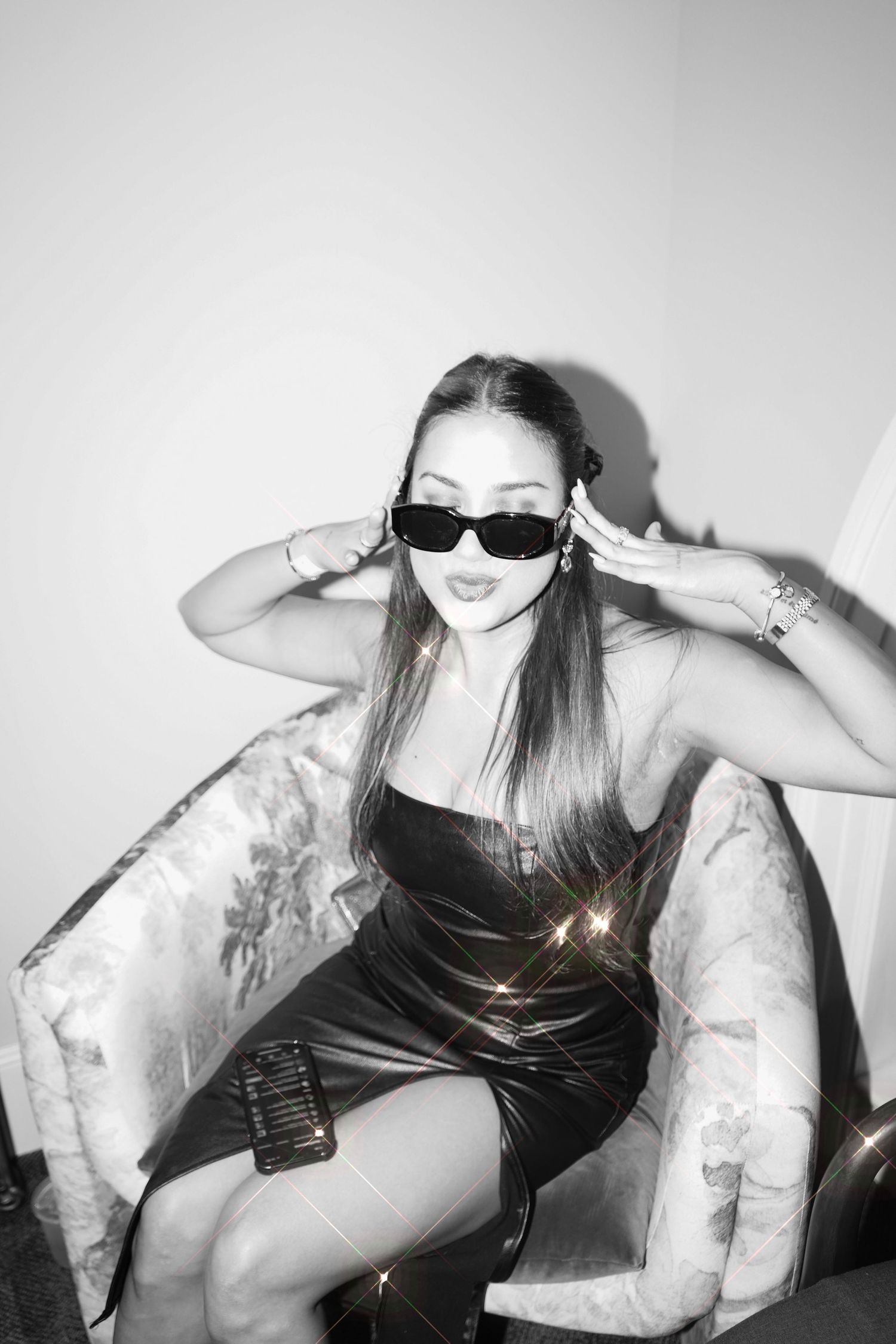 Stylish person in black dress and sunglasses poses on white couch in monochrome photo.