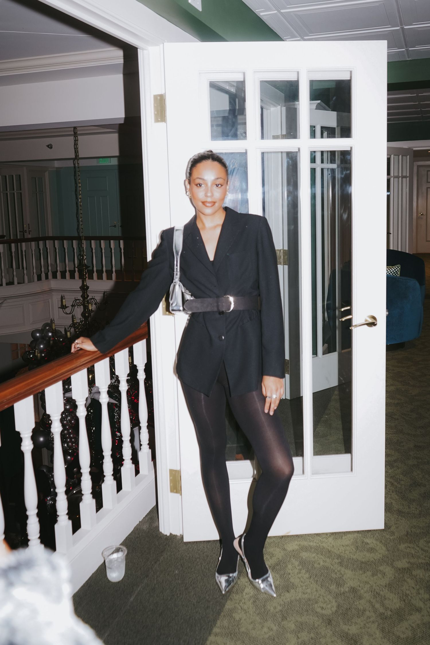 A person in all black business attire poses confidently in a doorway with white trim.