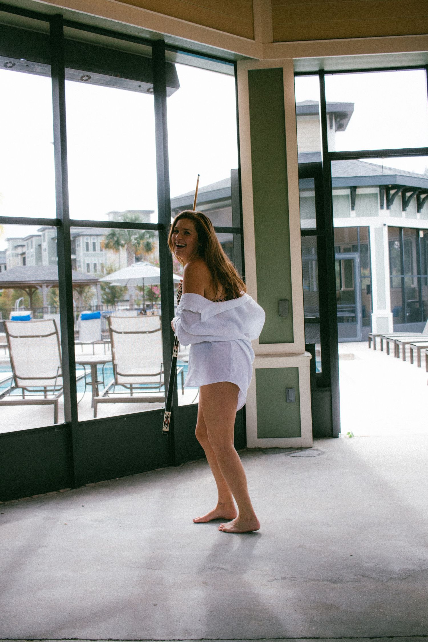 Person in white shirt posing playfully near large windows in a recreational area.
