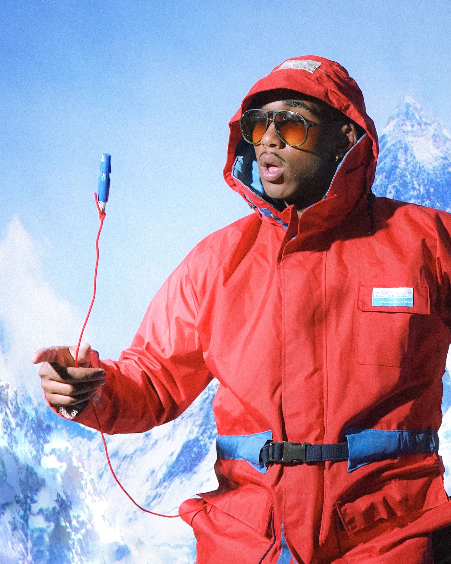 Person in bright red winter gear holds equipment against snowy mountain backdrop.