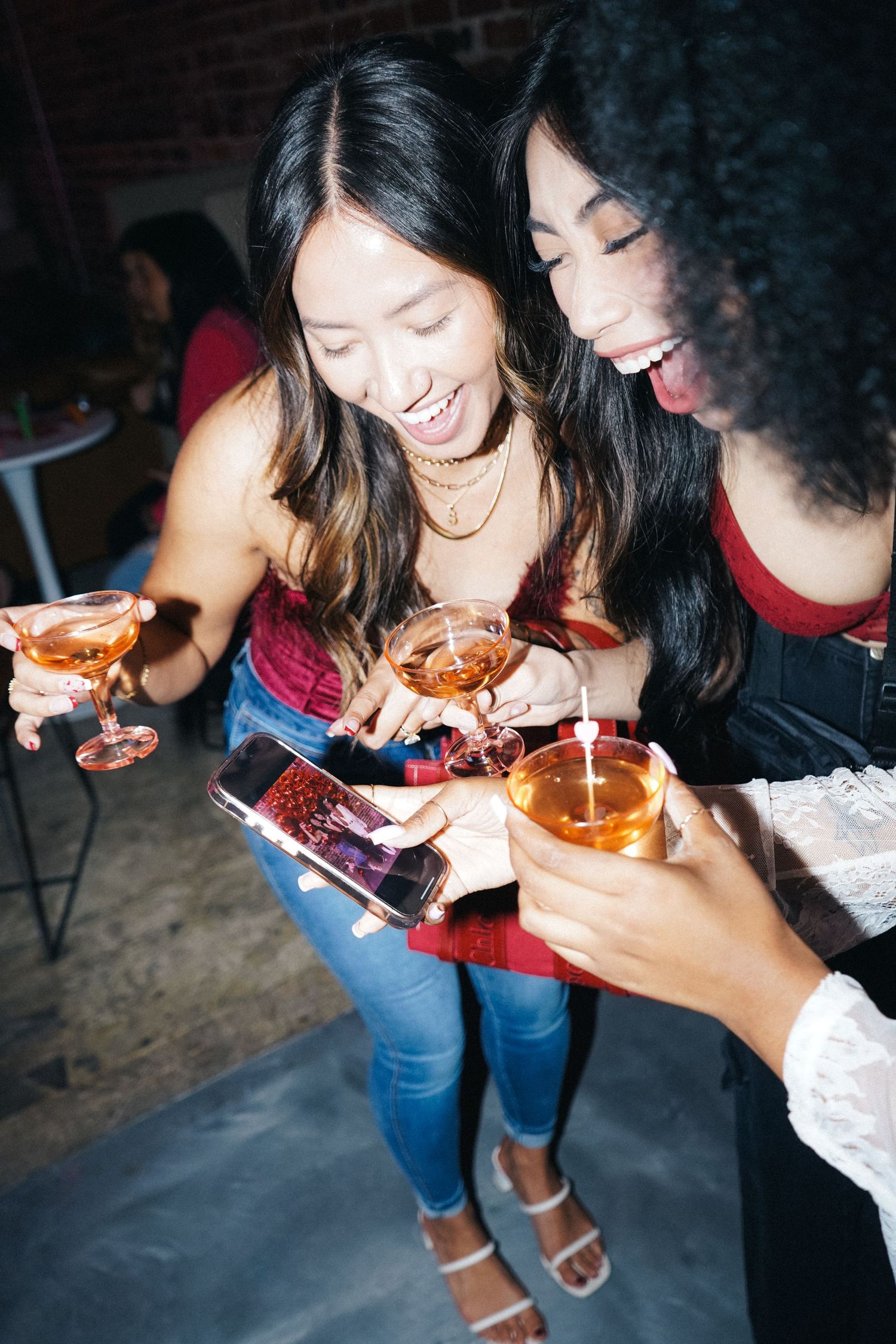 Friends sharing drinks and laughing while looking at phone at party.