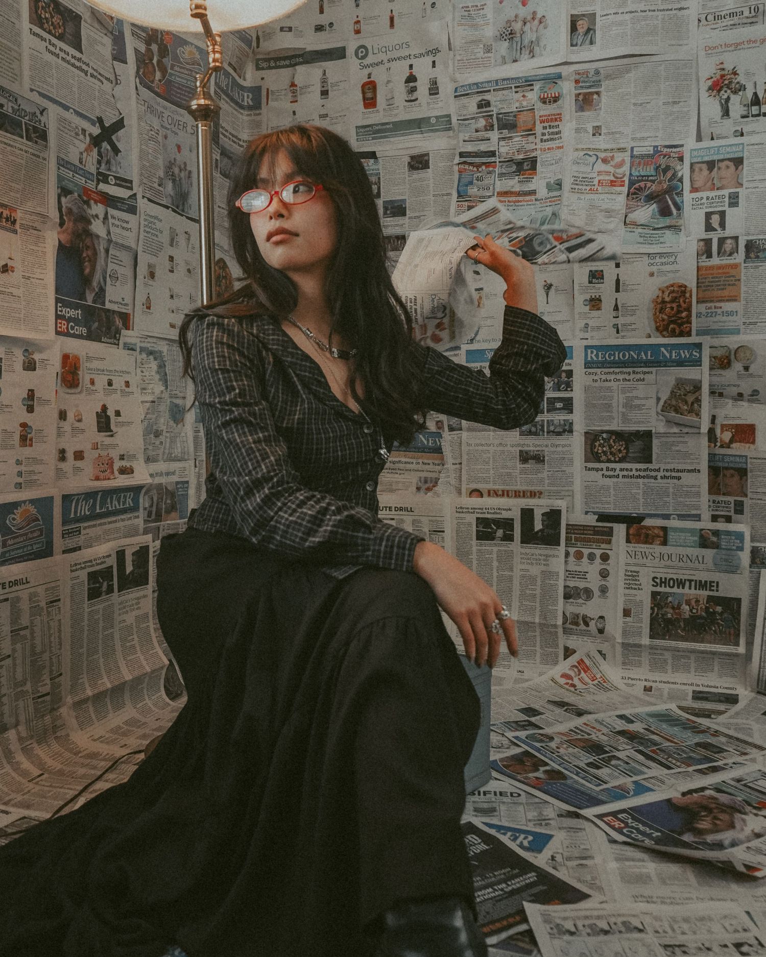 Artistic portrait against wall covered in vintage newspaper clippings and advertisements.
