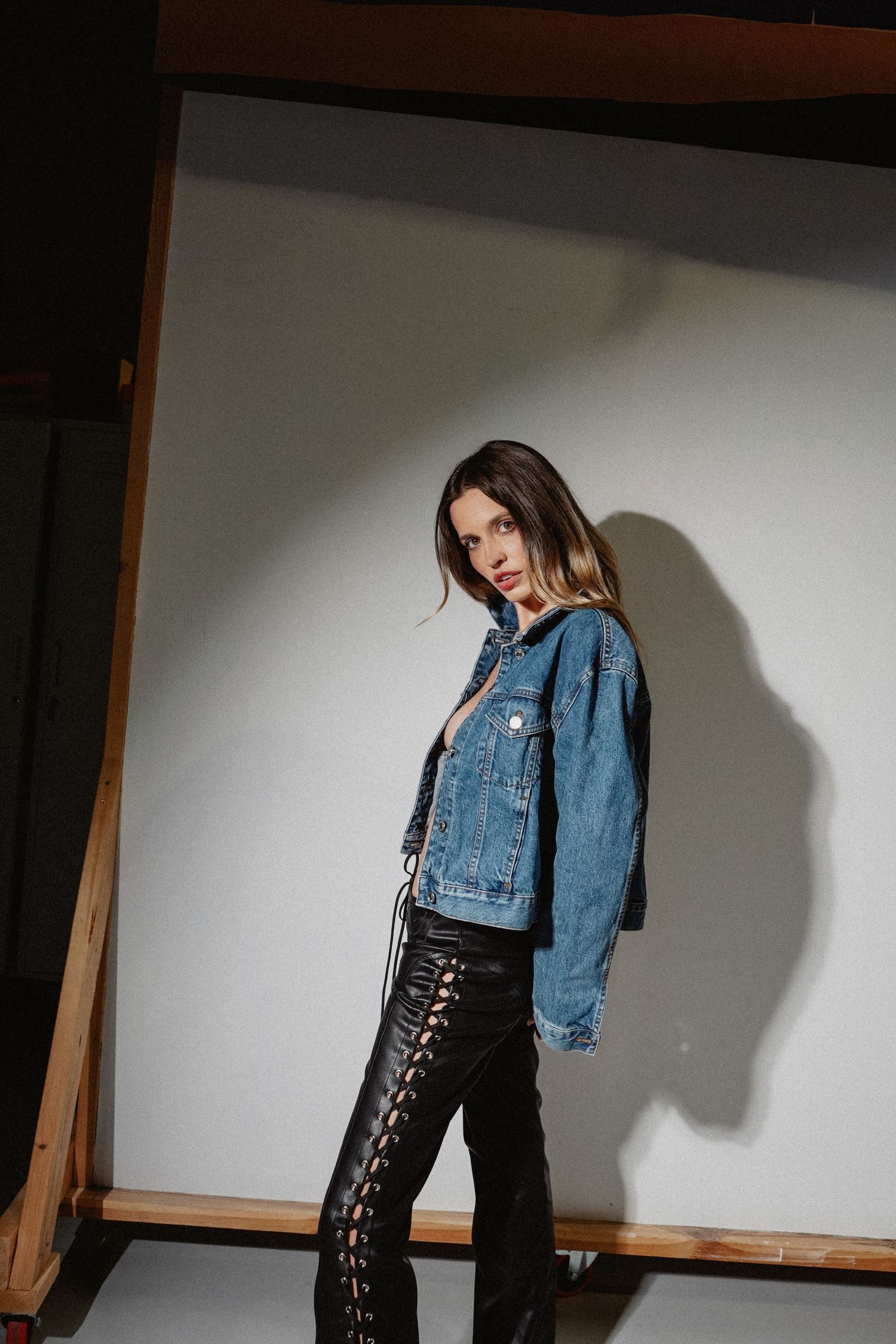 Edgy fashion pose showcasing denim jacket and lace-up leather pants.