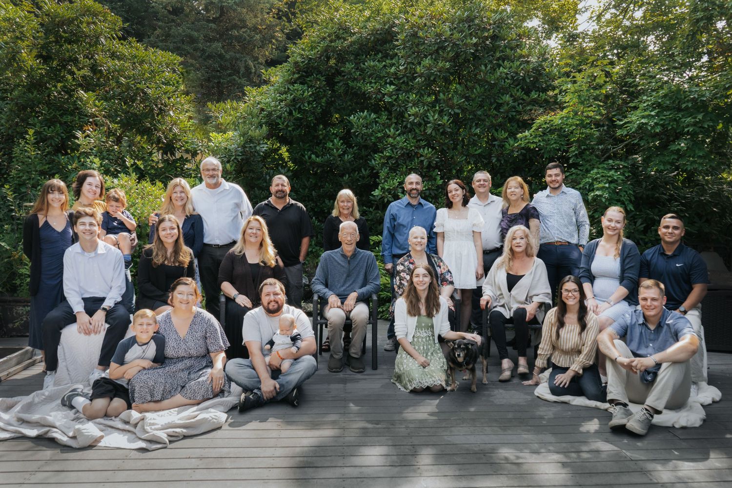 Large group photo of people gathered outdoors on wooden deck for formal portrait.