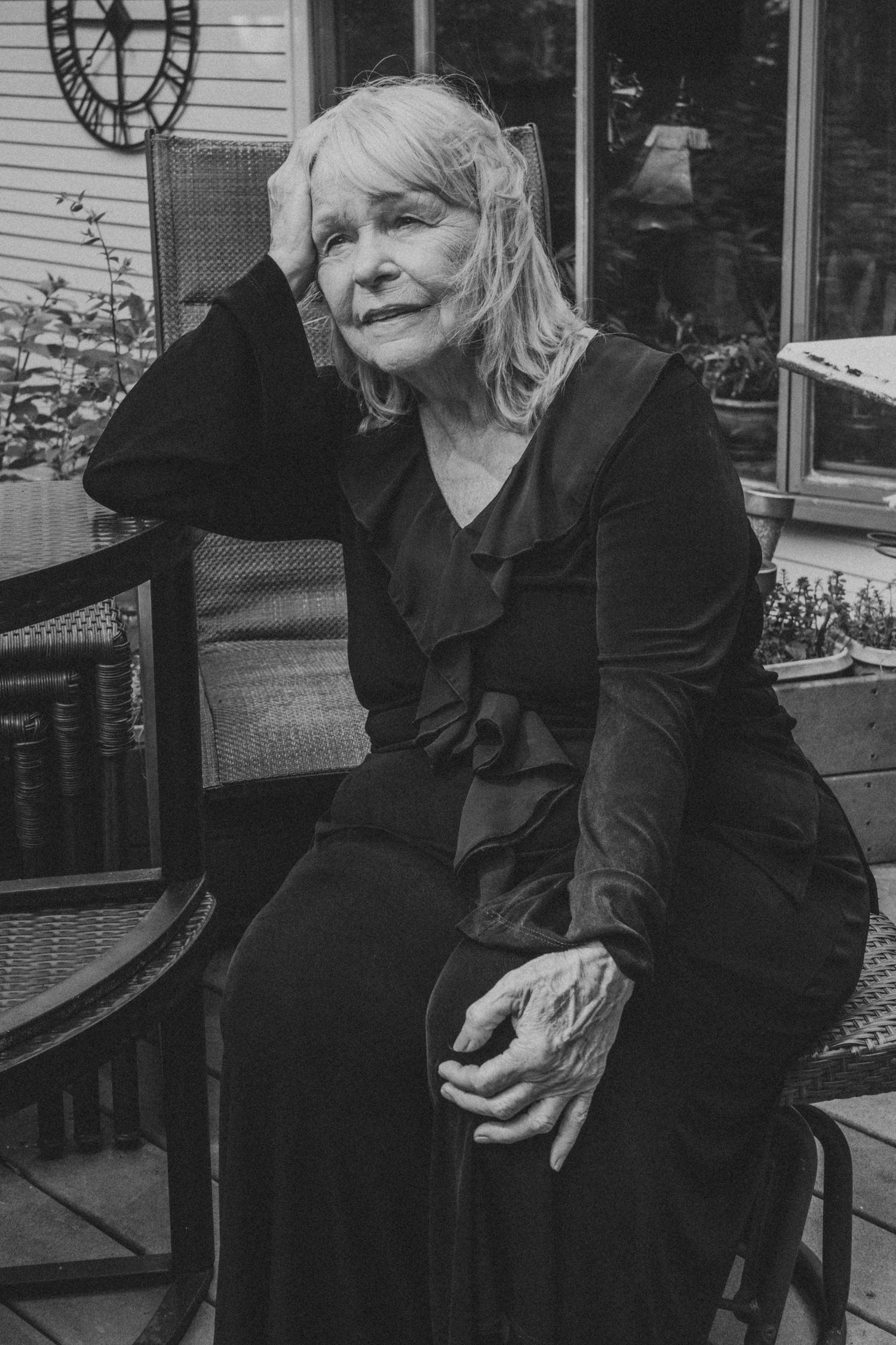 Atmospheric black and white portrait of person in dark clothing sitting on porch.