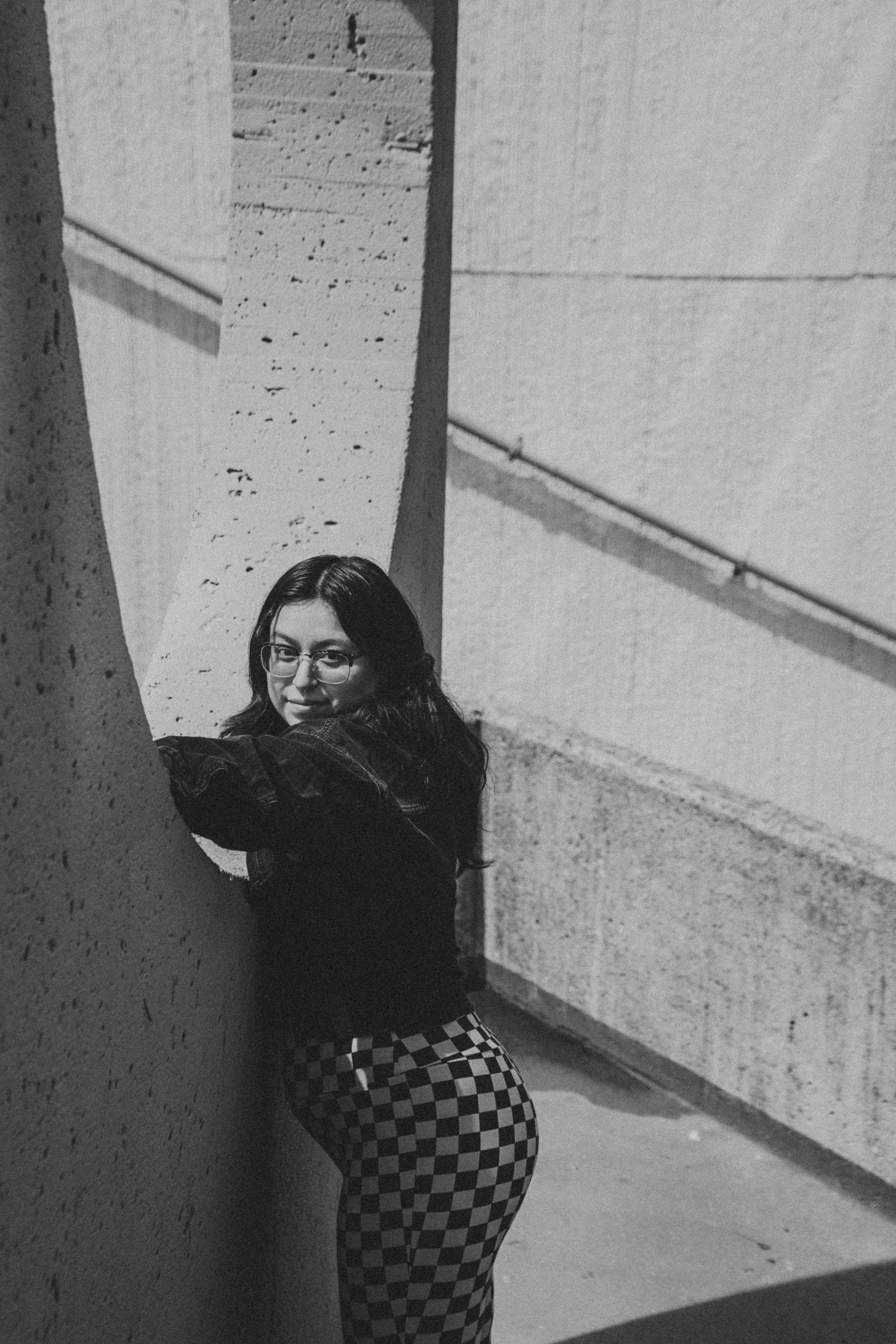 Black and white photo of someone in checkered pants posing against concrete wall.