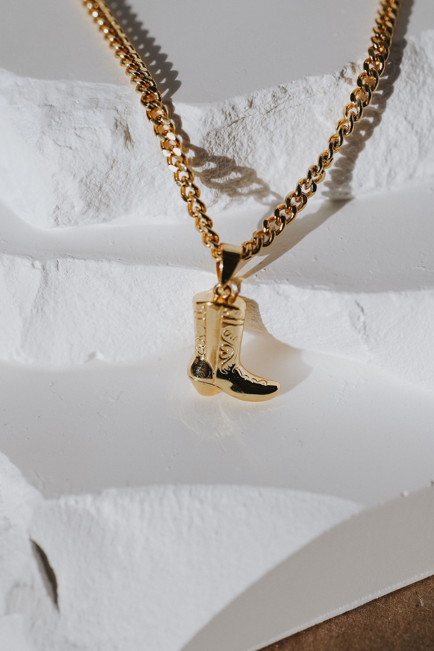 Gold chain necklace with boot charm pendant photographed on white textured background.