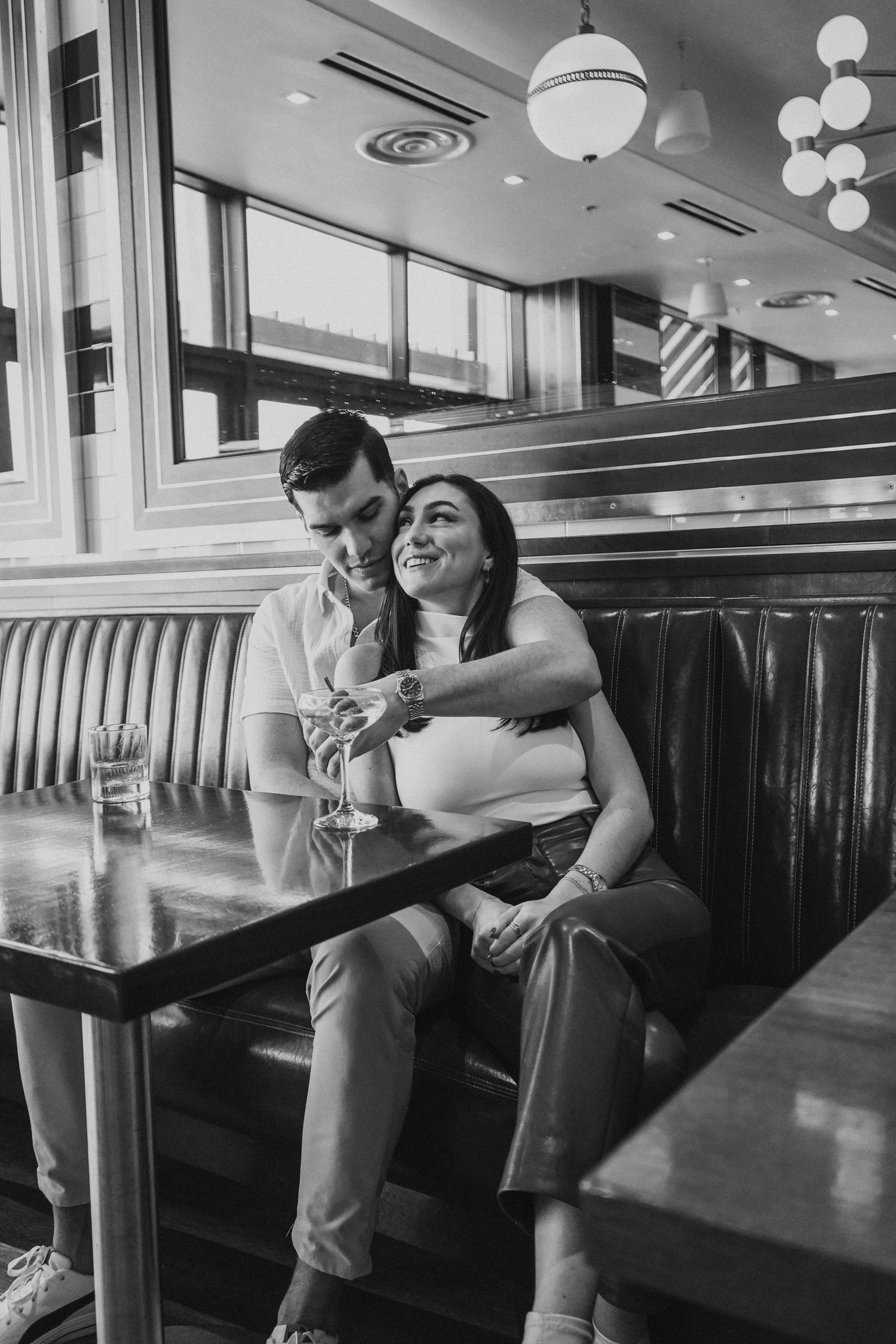 A black and white photo of a couple sharing a playful moment in a retro diner booth.