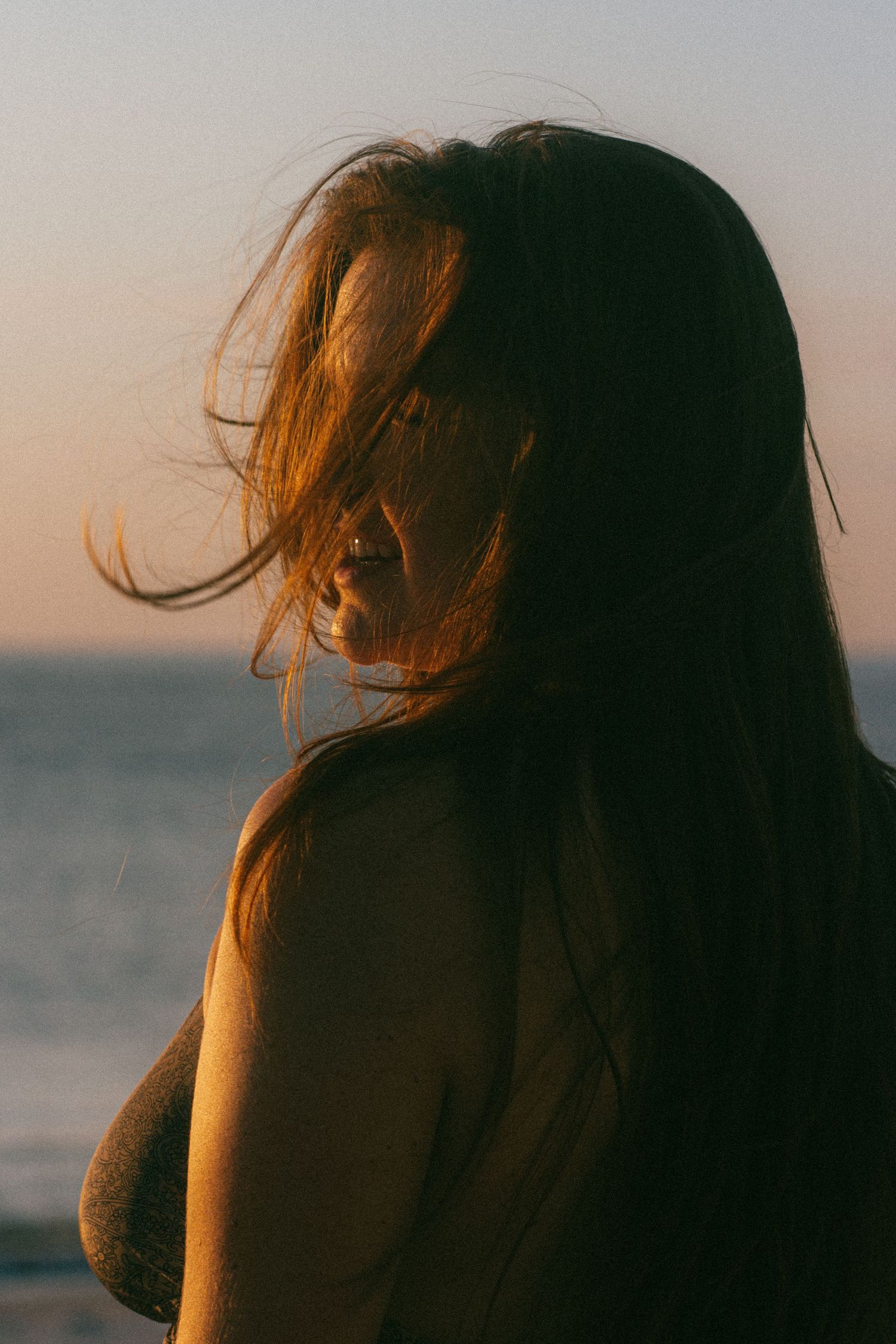 Backlit silhouette of person with windswept hair against ocean horizon.