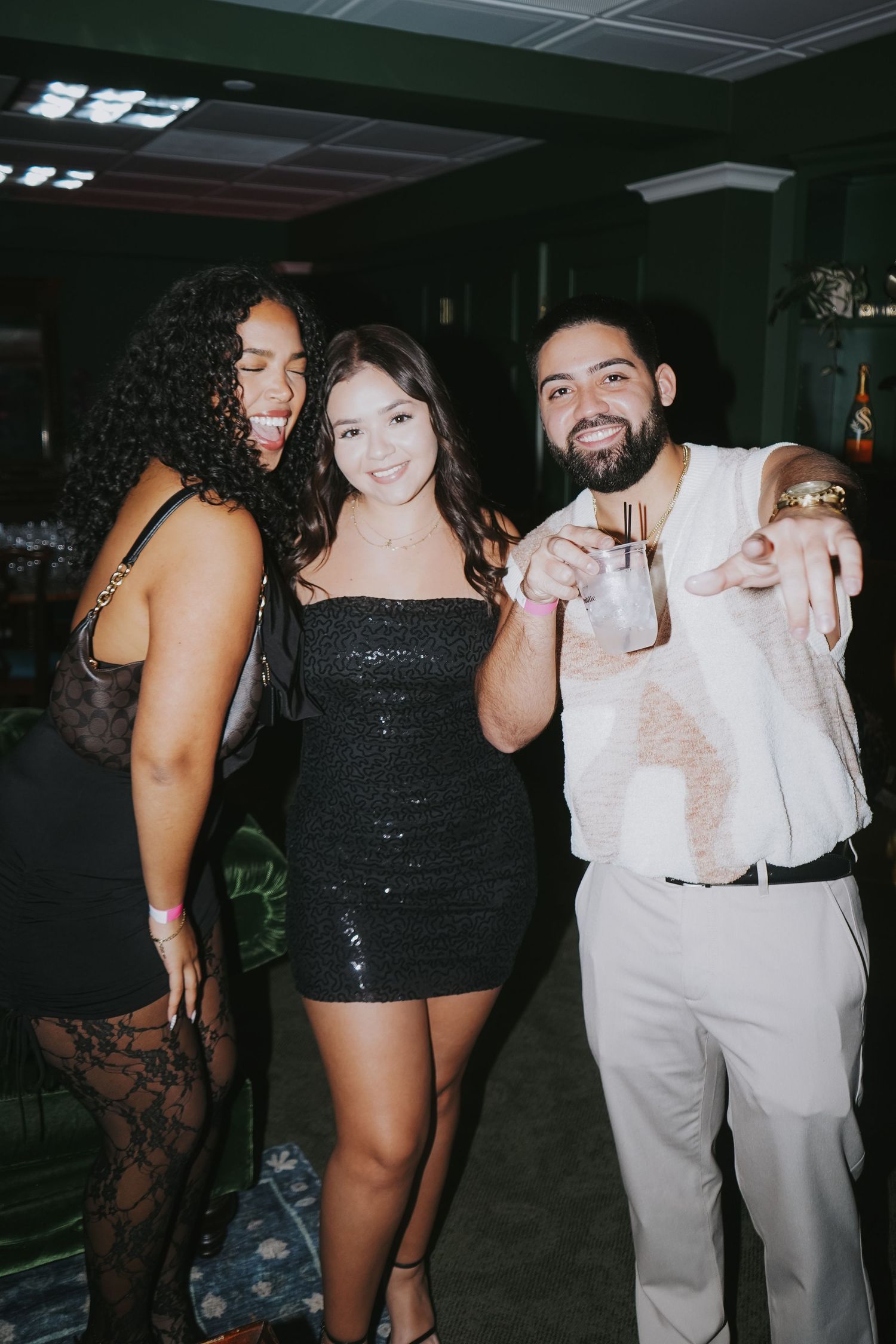 Three friends pose together at a nightclub, wearing stylish outfits for a fun evening out.