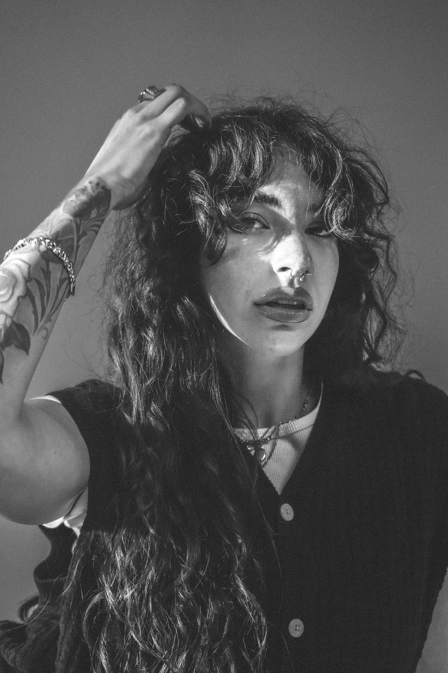 Black and white portrait of figure with long dark curly hair in dramatic lighting.