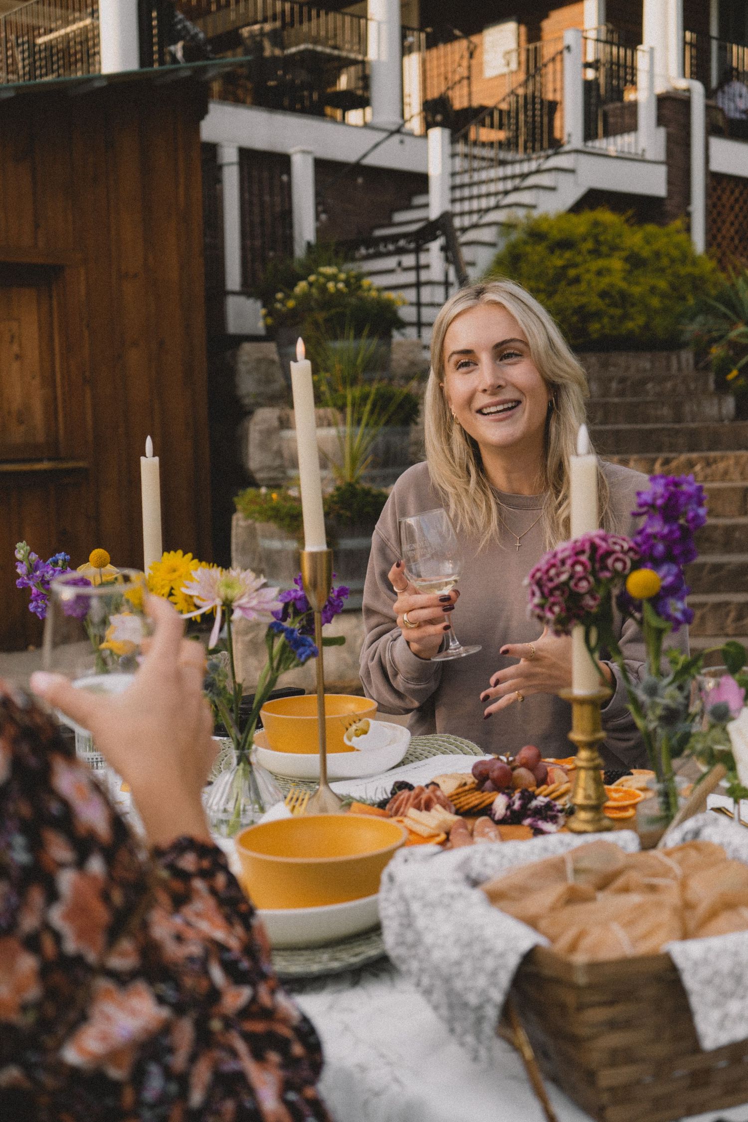Outdoor dining scene with colorful flowers, wine glasses, and fresh food on a marble table.