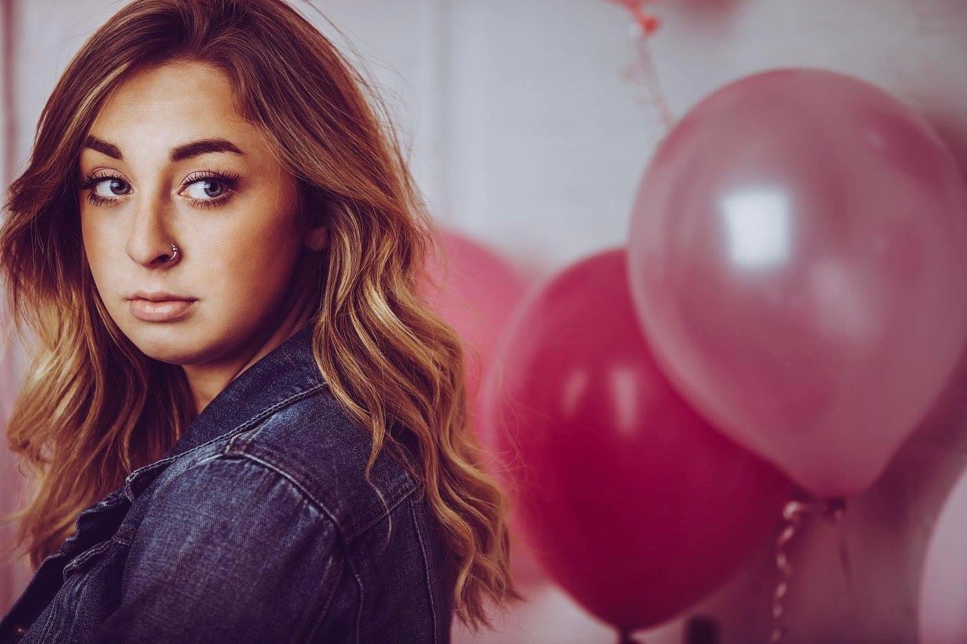 Portrait with denim jacket against pink balloon background.