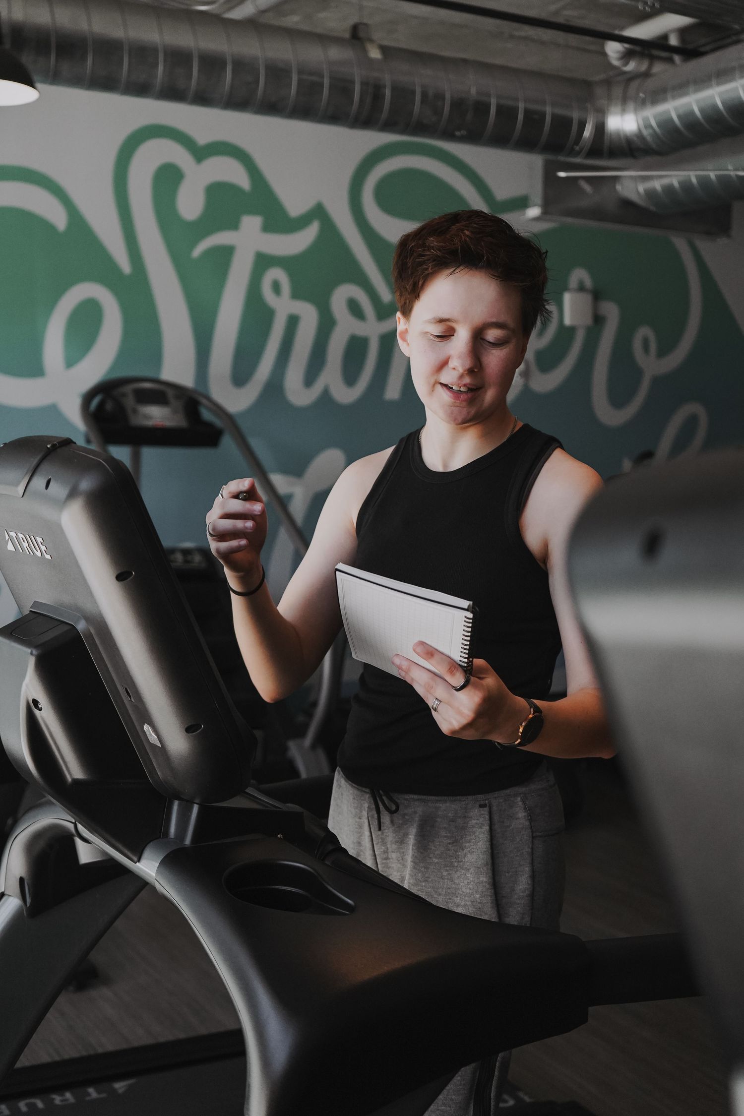 Person checking fitness notes while standing next to exercise equipment.
