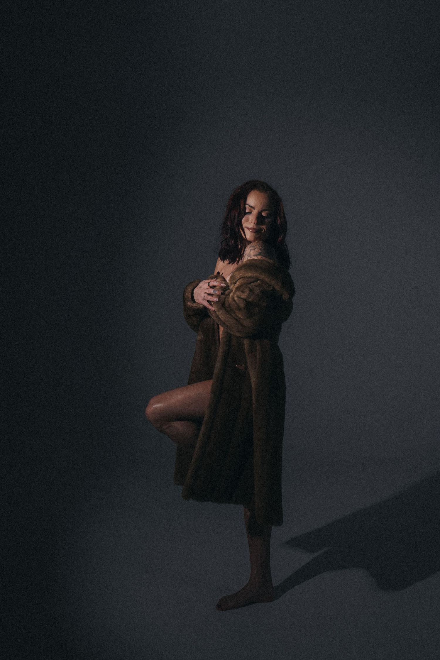 Silhouette pose against dark background wearing brown fur coat.