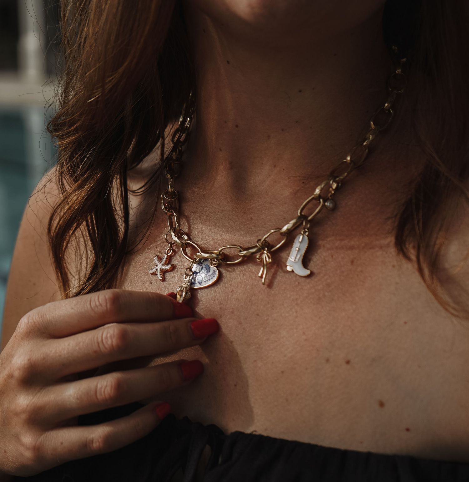 Gold charm necklace featuring multiple small decorative pendants worn with black top.