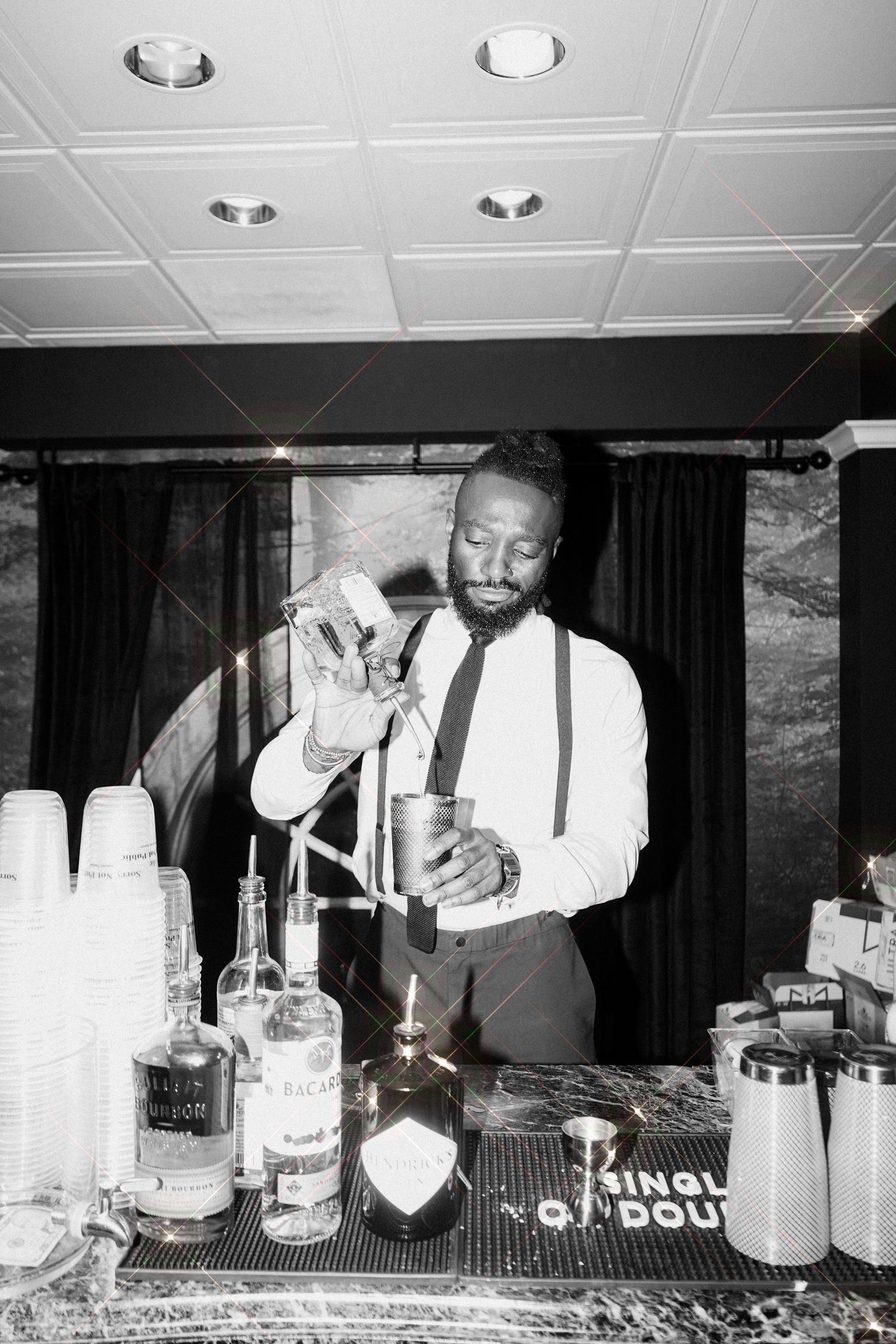 Bartender in suspenders pouring drinks at black and white event.