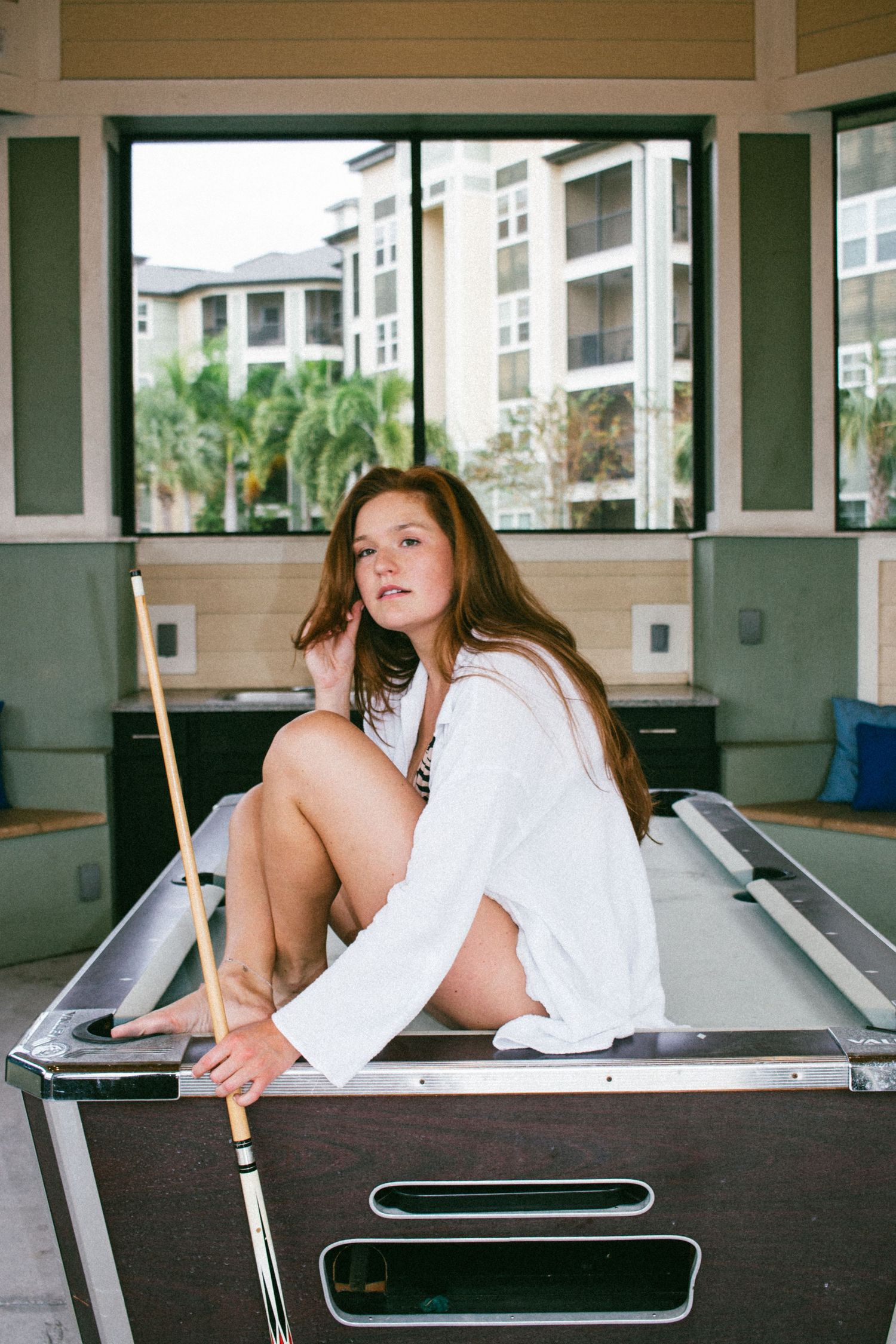 Casual portrait on pool table in game room with apartment view through windows.