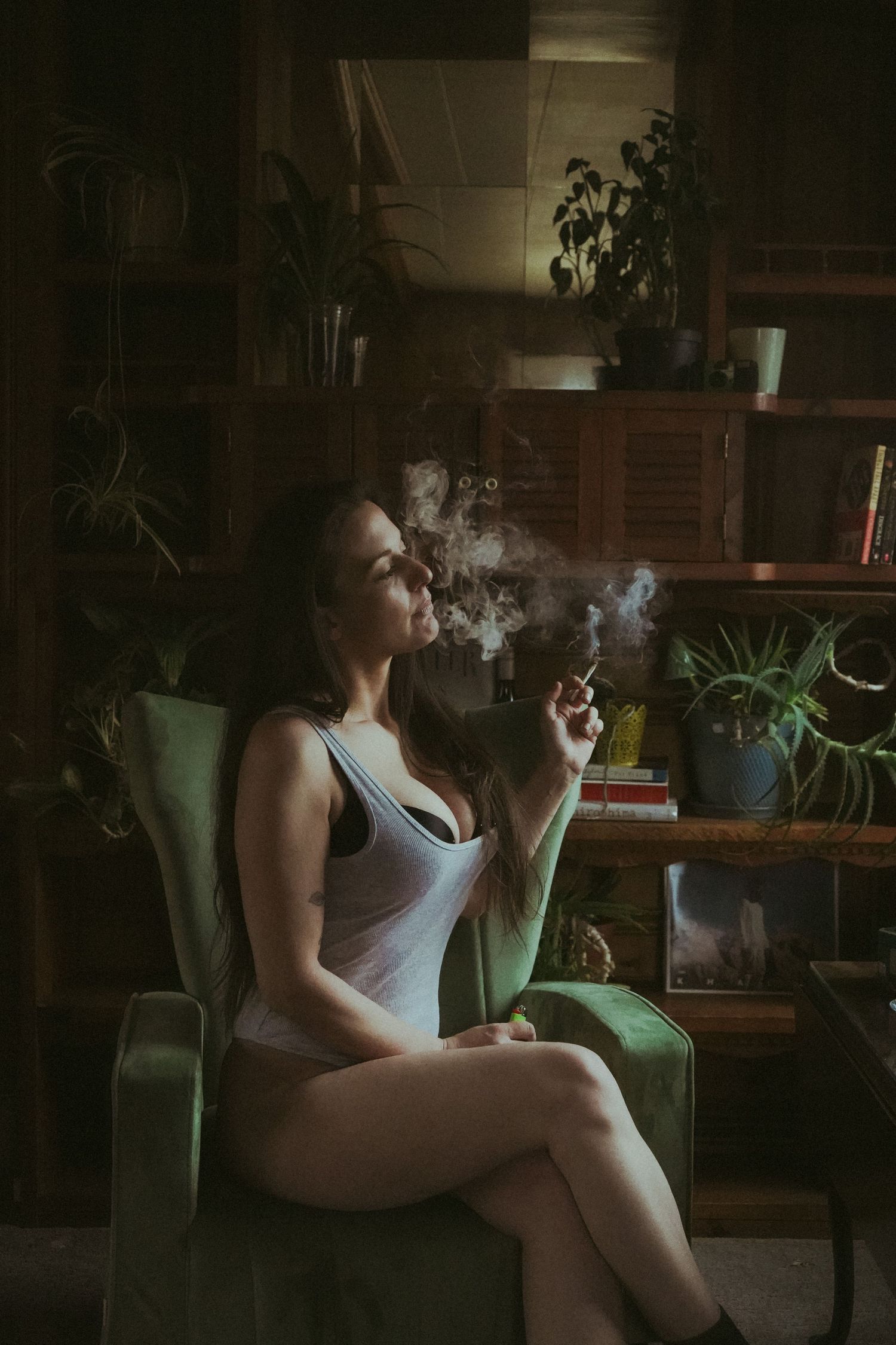 Moody portrait in vintage chair with smoke and plants in background.