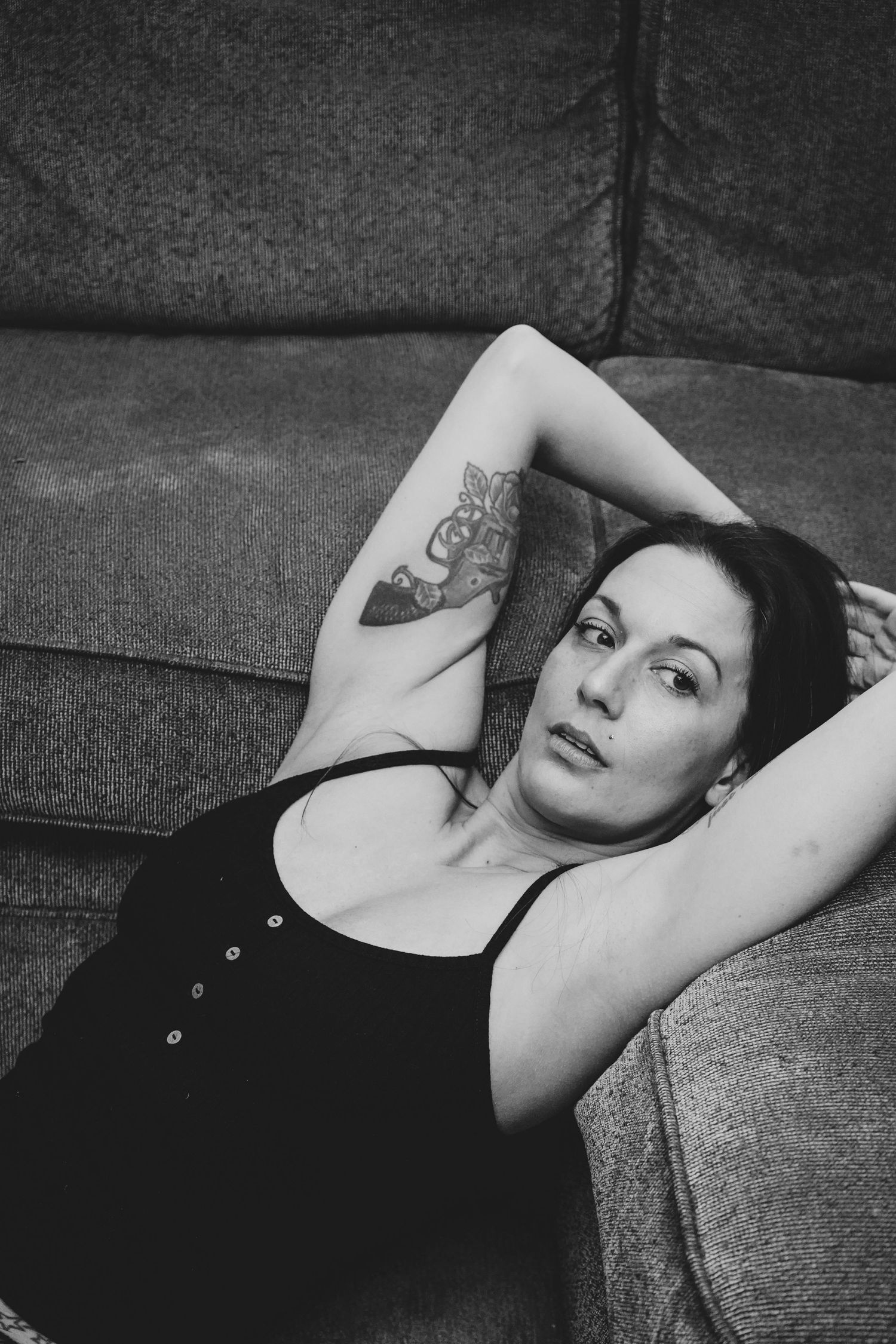 Casual lounging portrait showing arm tattoo detail against gray couch.