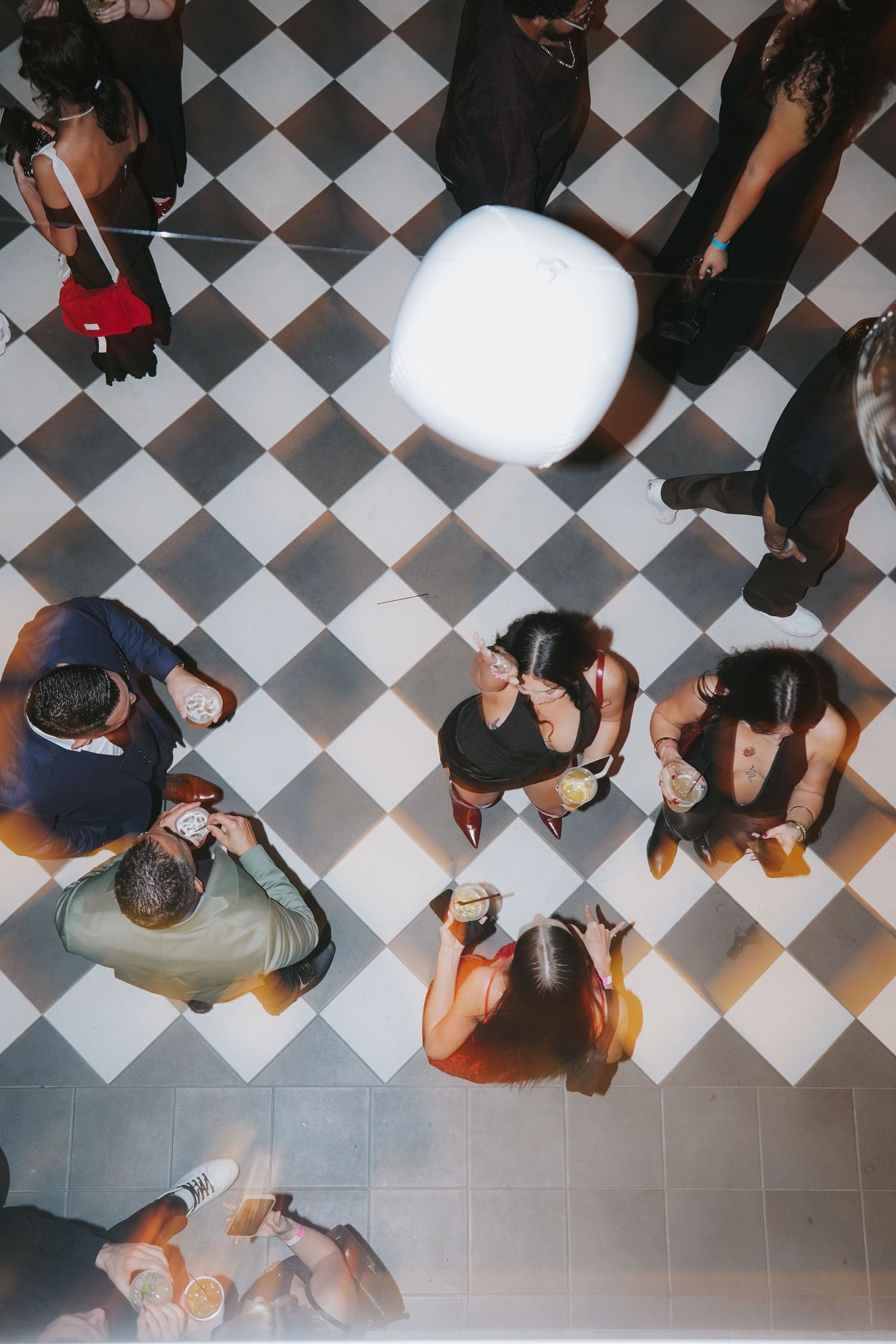 Birds-eye view of party guests gathered around a white circular table on checkered flooring.