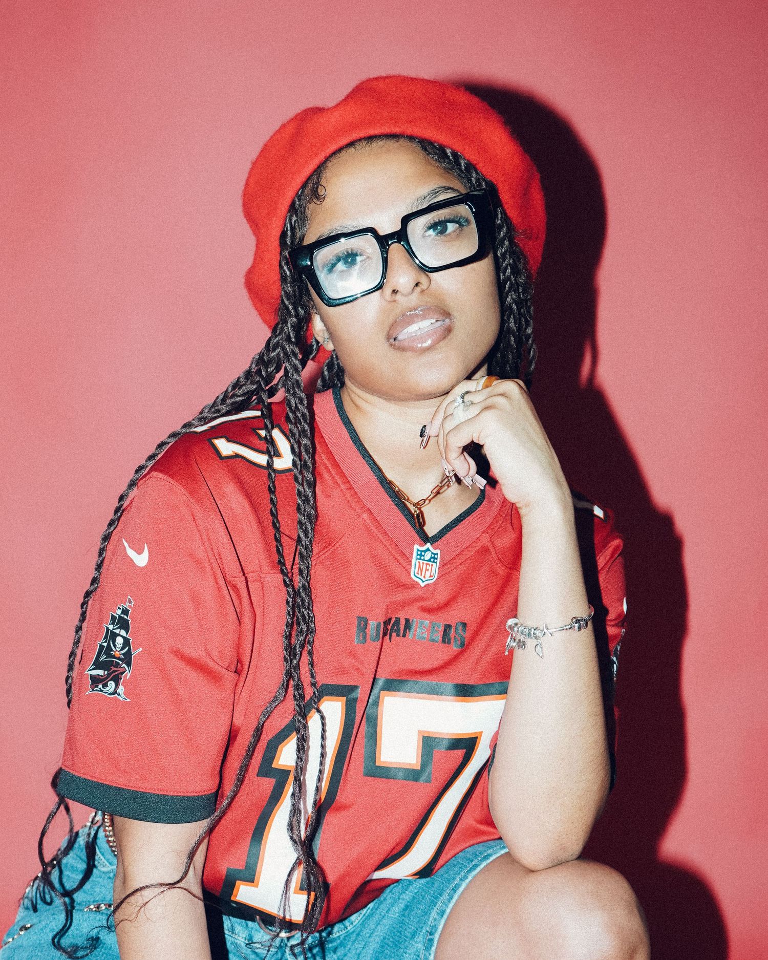 Portrait against pink background wearing red sports jersey and black-rimmed glasses.