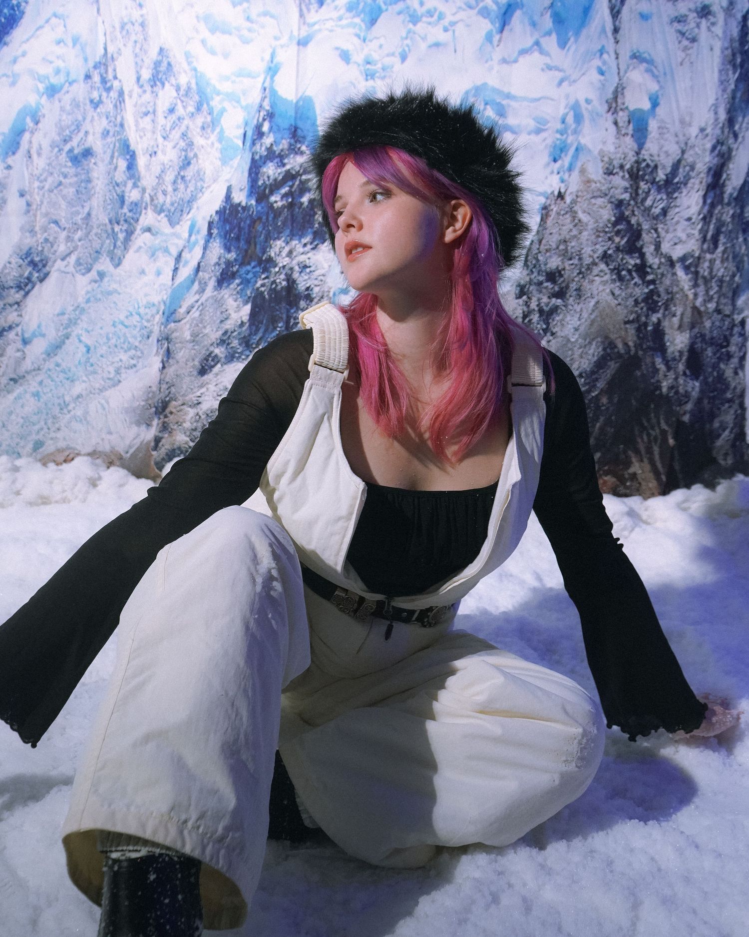 Model in black and white outfit poses on snow with mountain backdrop.