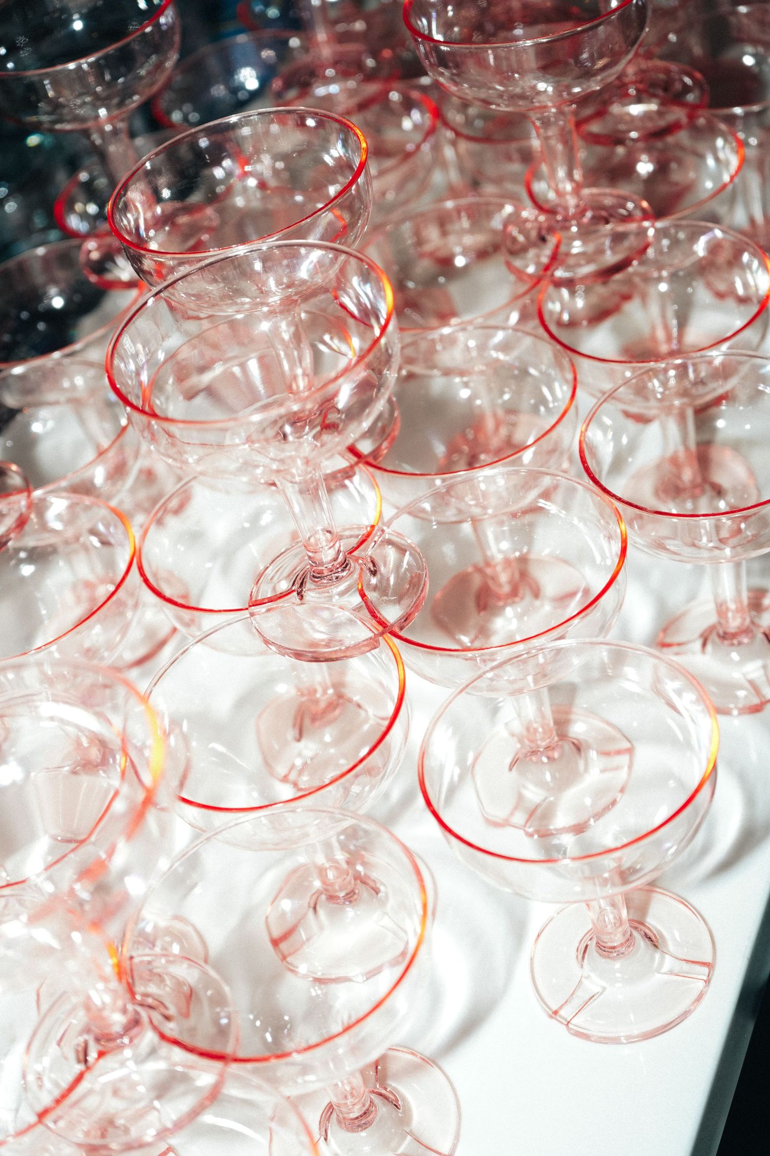 Rows of empty champagne coupes arranged on white surface with pink lighting.