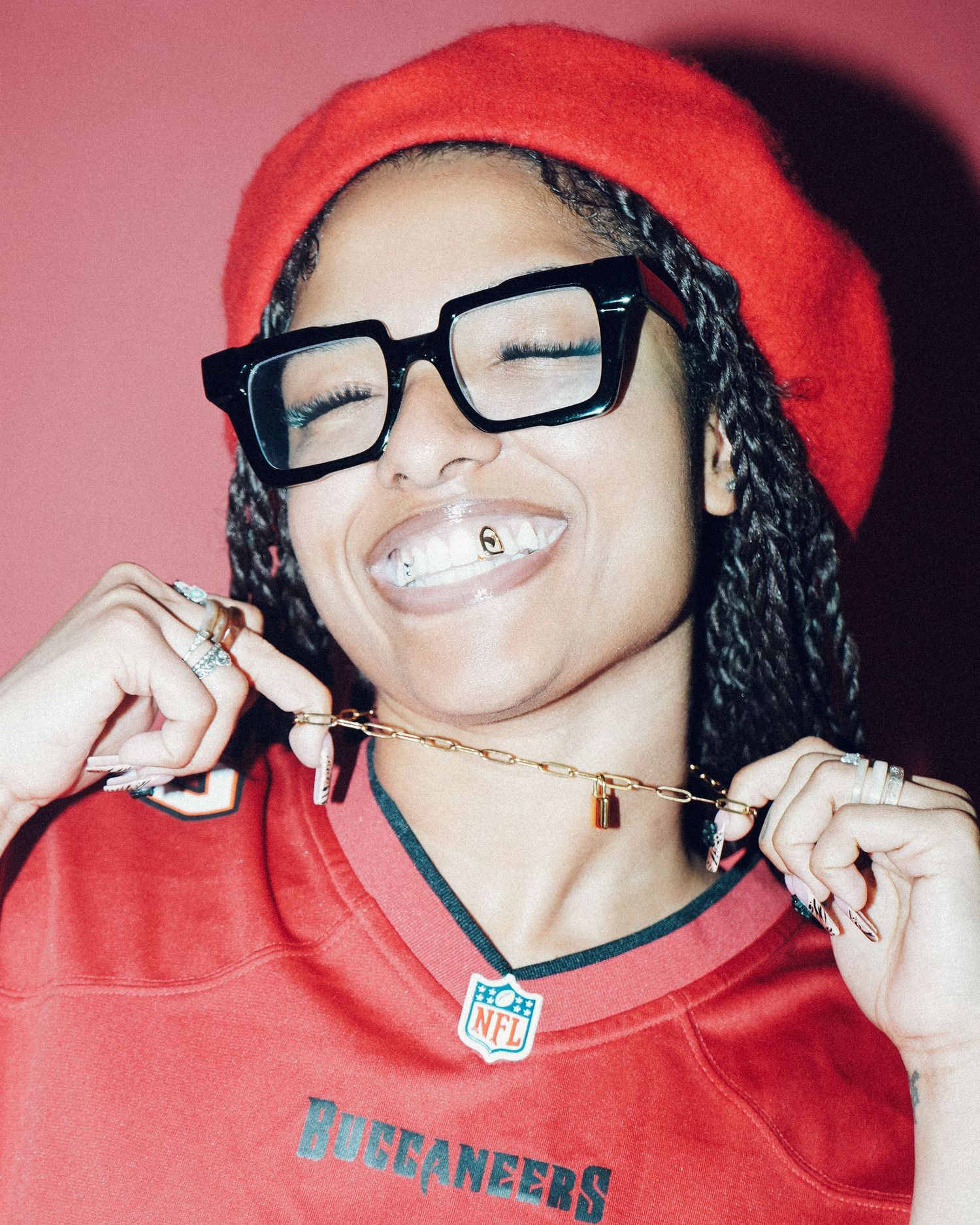 Vibrant portrait of person in red beanie and Buccaneers jersey against pink background.