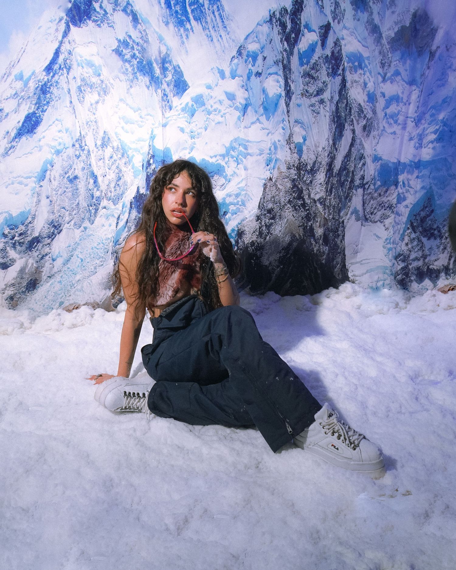 Model poses on snow-covered ground with dramatic mountain peaks in background.