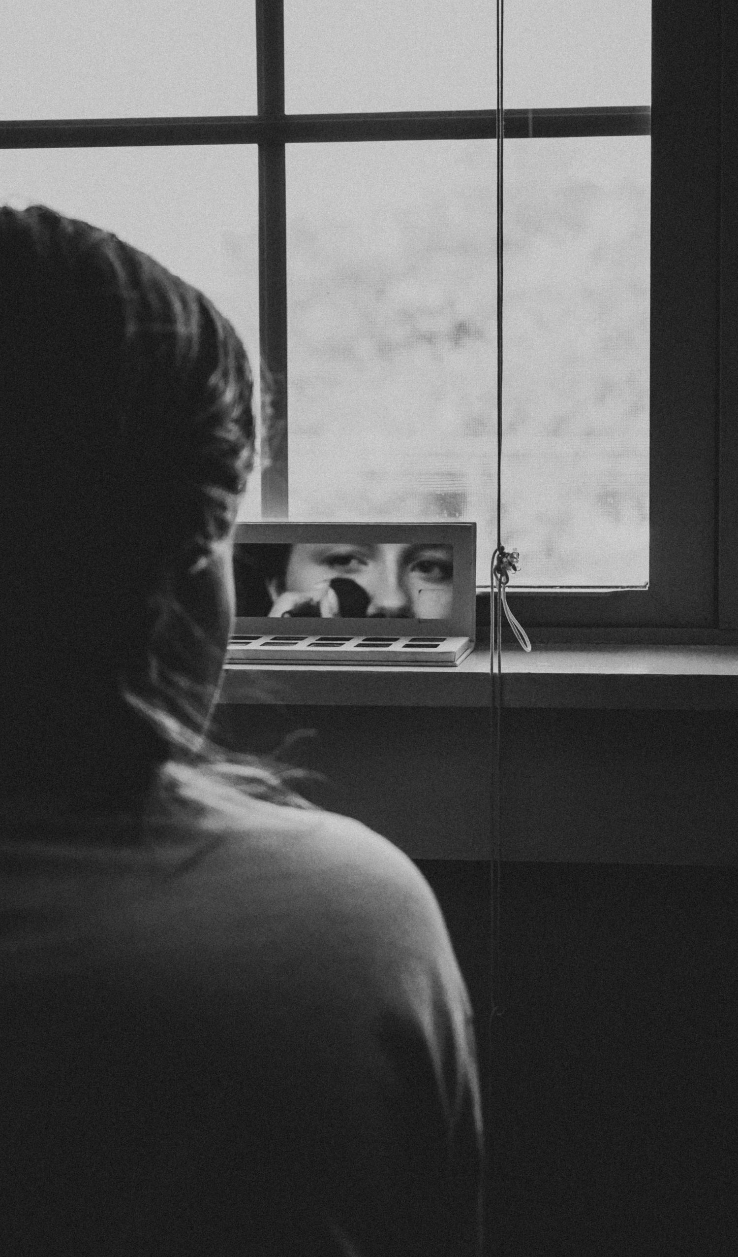 Silhouetted figure looking out of a window in a moody black and white composition.