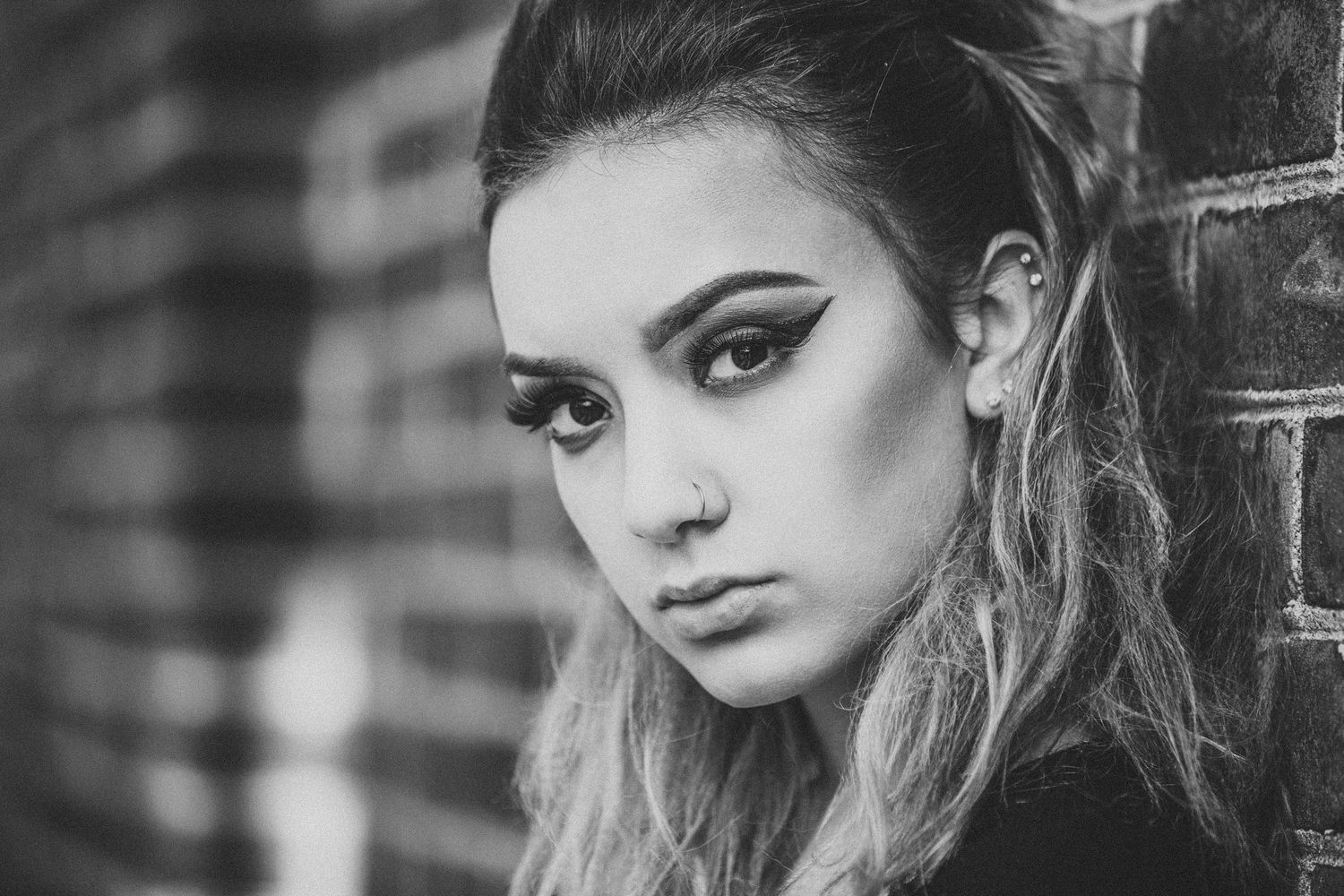 Close-up portrait with dramatic eye makeup against brick wall background.