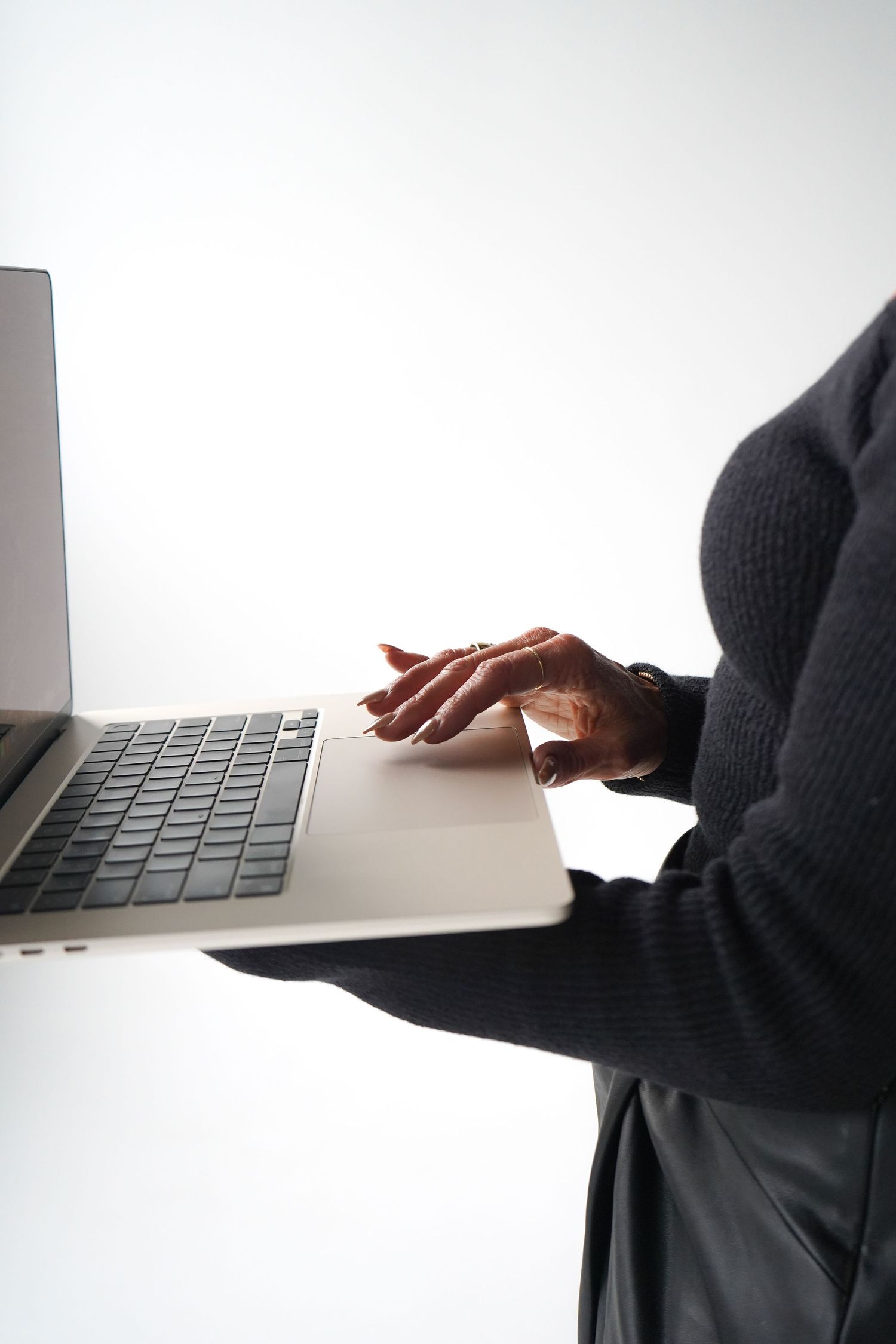 Close-up view of hands typing on a silver laptop keyboard against a white background.