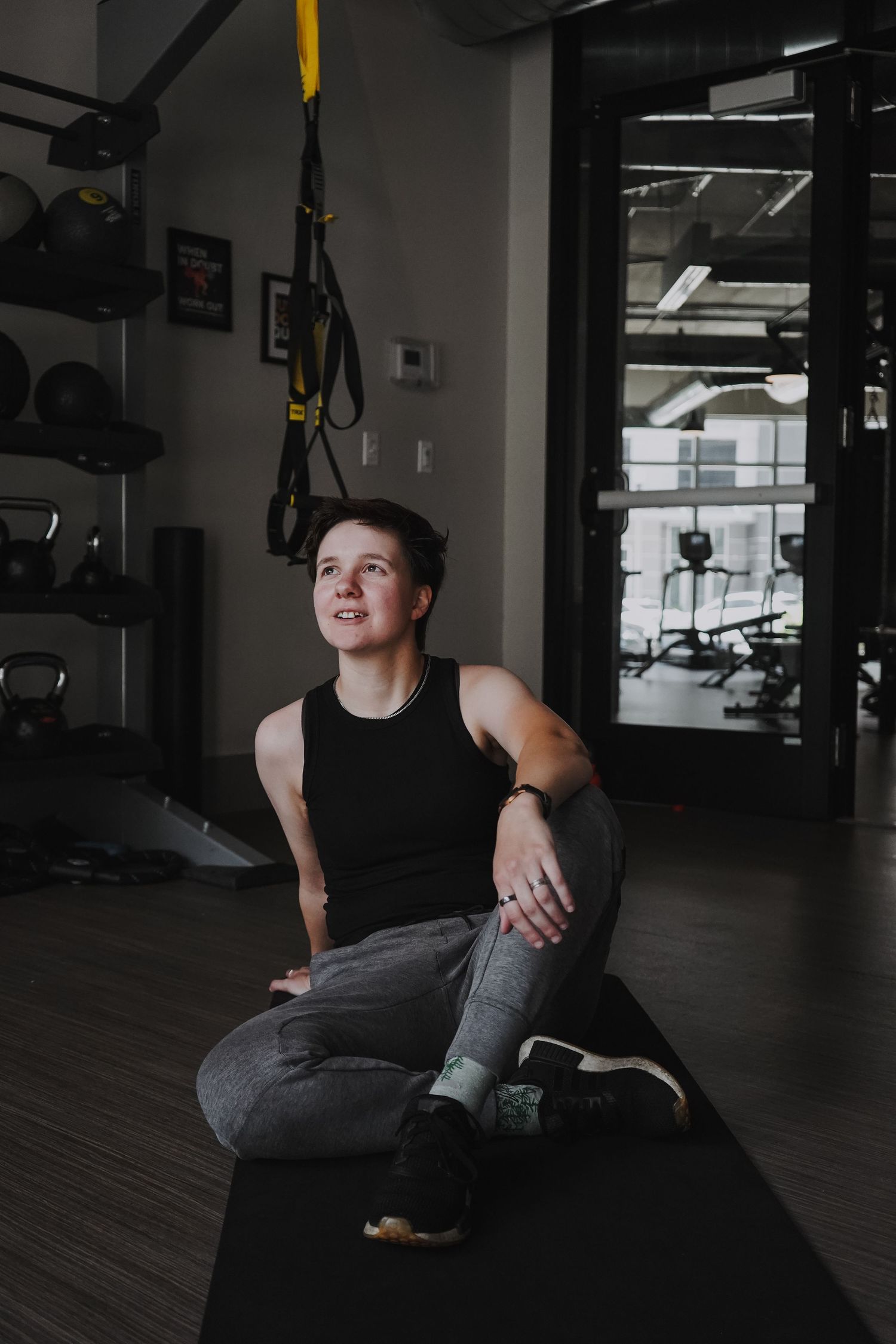 Person sitting on exercise mat near TRX suspension equipment in modern gym.